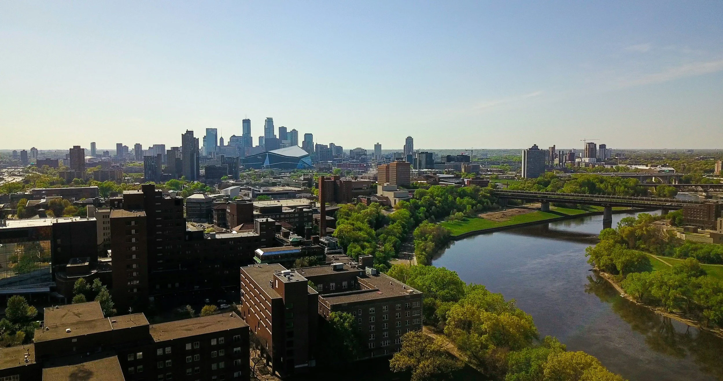 A panoramic view of a city skyline with skyscrapers, a river in the foreground, and a clear blue sky.