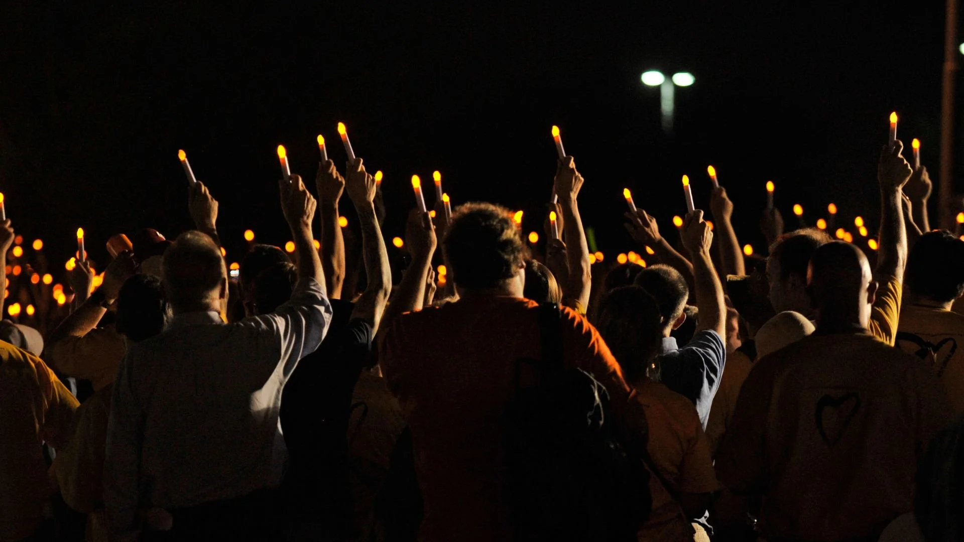 Crowd of people holding lit candles at night, participating in a vigil or memorial event.