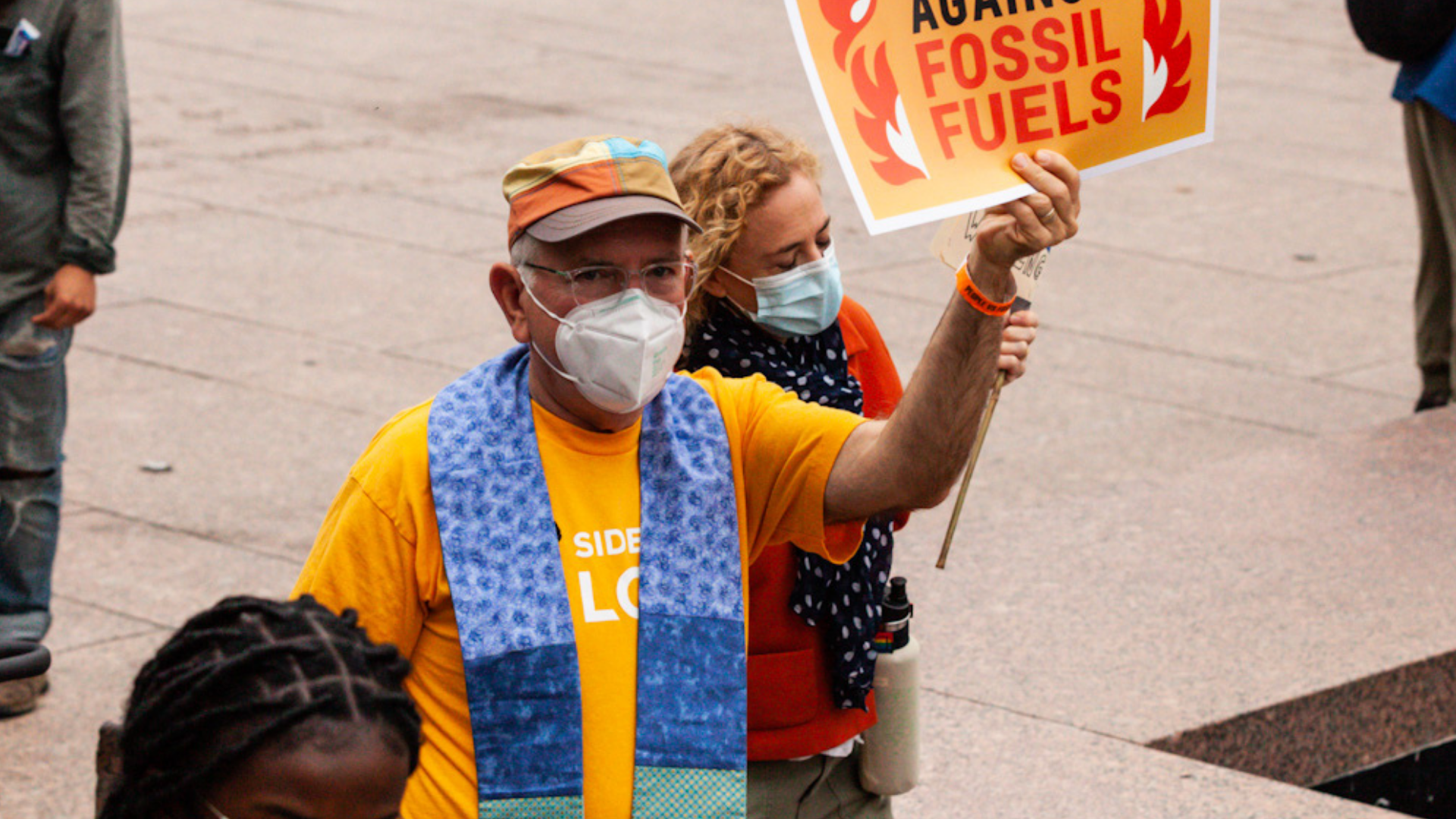 Protesters wearing masks, holding a sign that reads 'Against Fossil Fuels' at a climate rally.