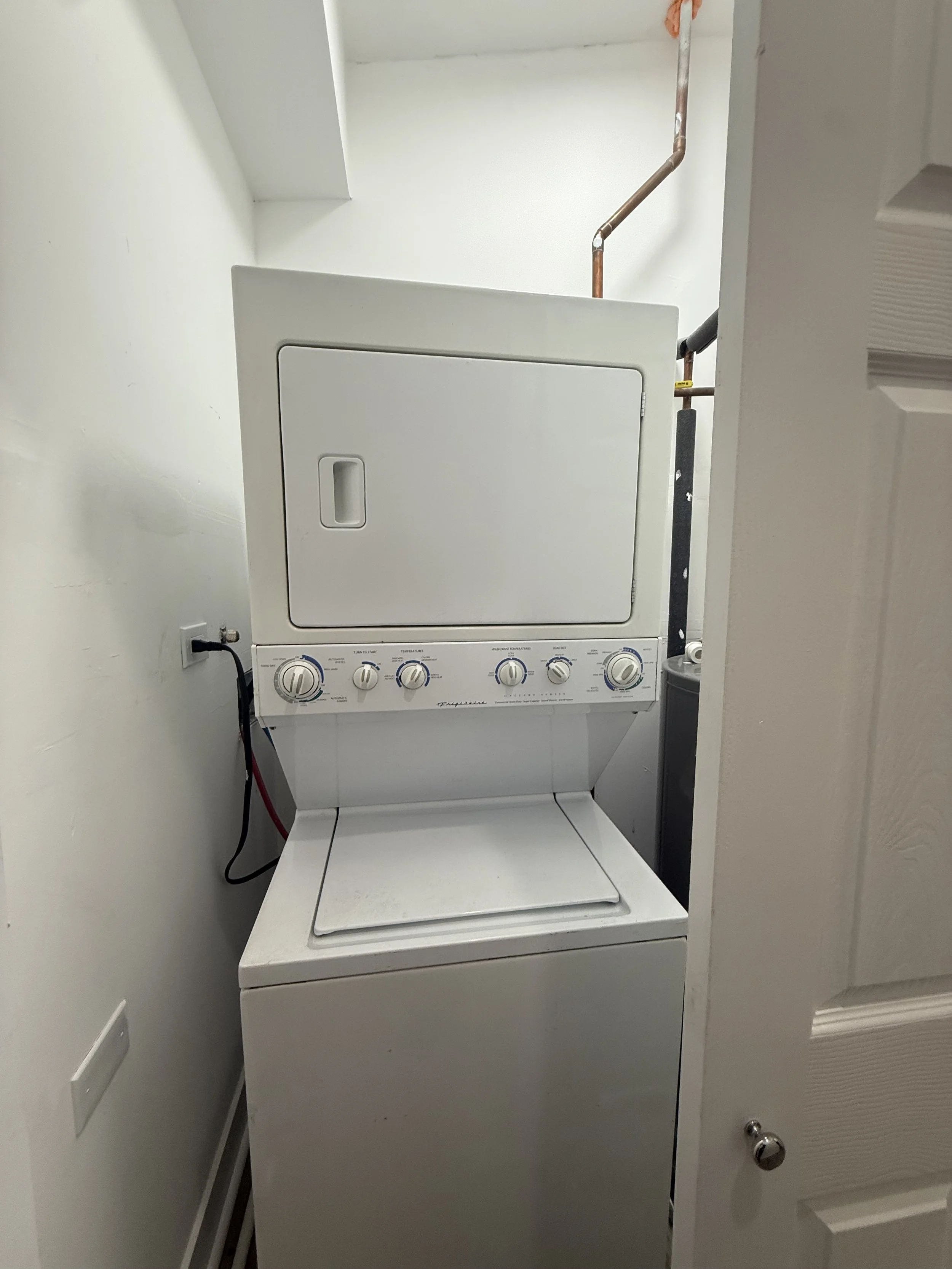 A white stacked washer and dryer unit in a laundry room, with the dryer on top and the washer below.
