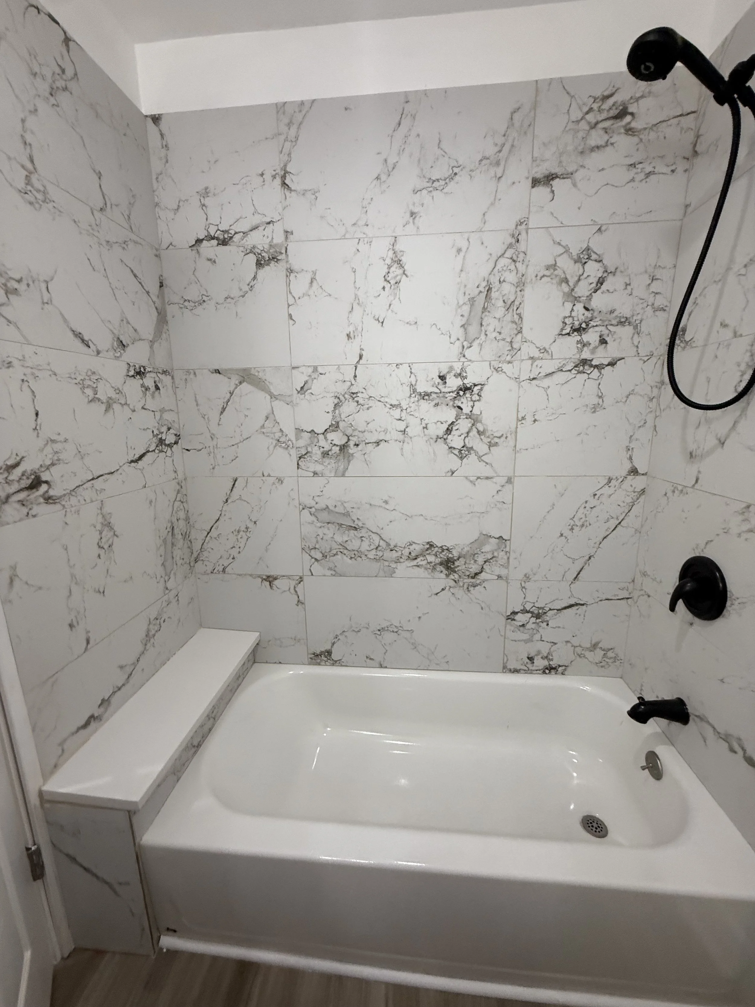 Bathroom shower area with white bathtub, marble wall tiles, black showerhead, and faucet.