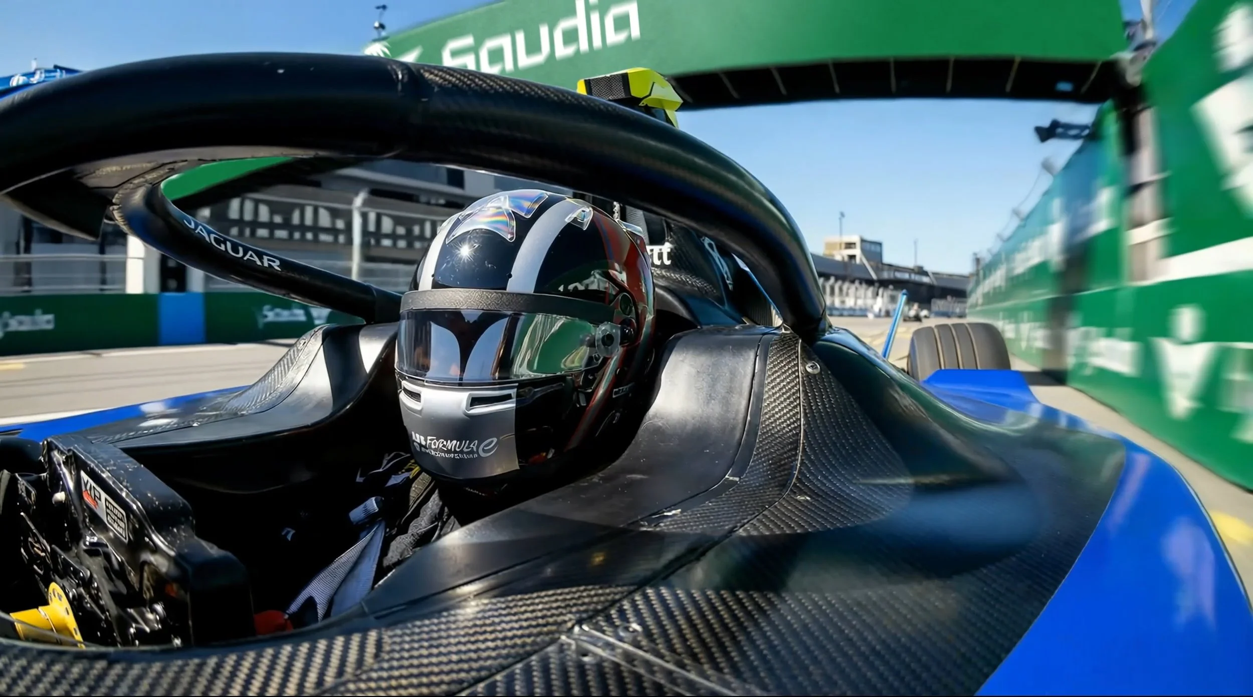 A first-person perspective from the cockpit of a Formula E racing car on a professional track under a clear sky.