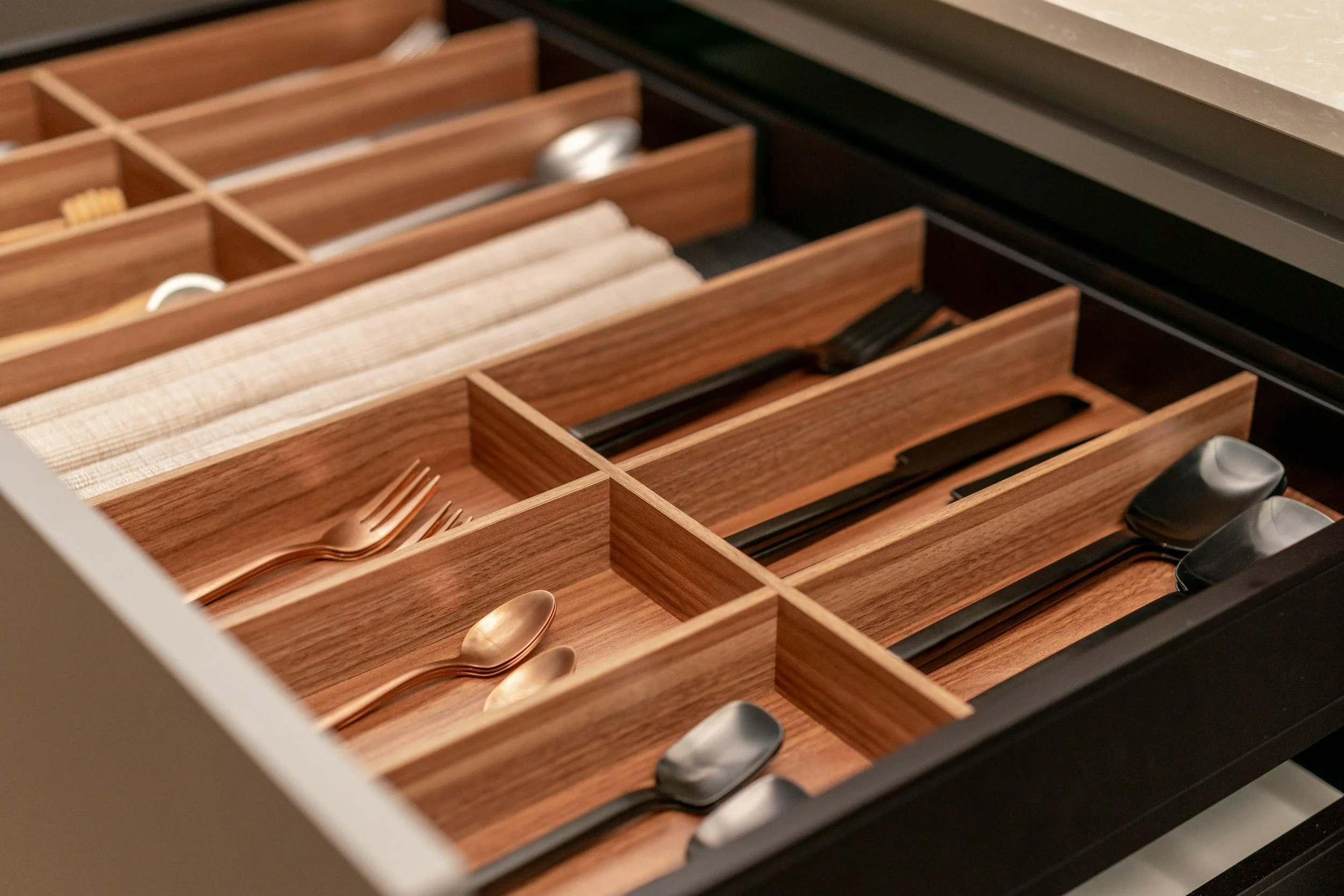 Drawer with organized compartments holding gold-colored utensils, black chopsticks, and small containers.