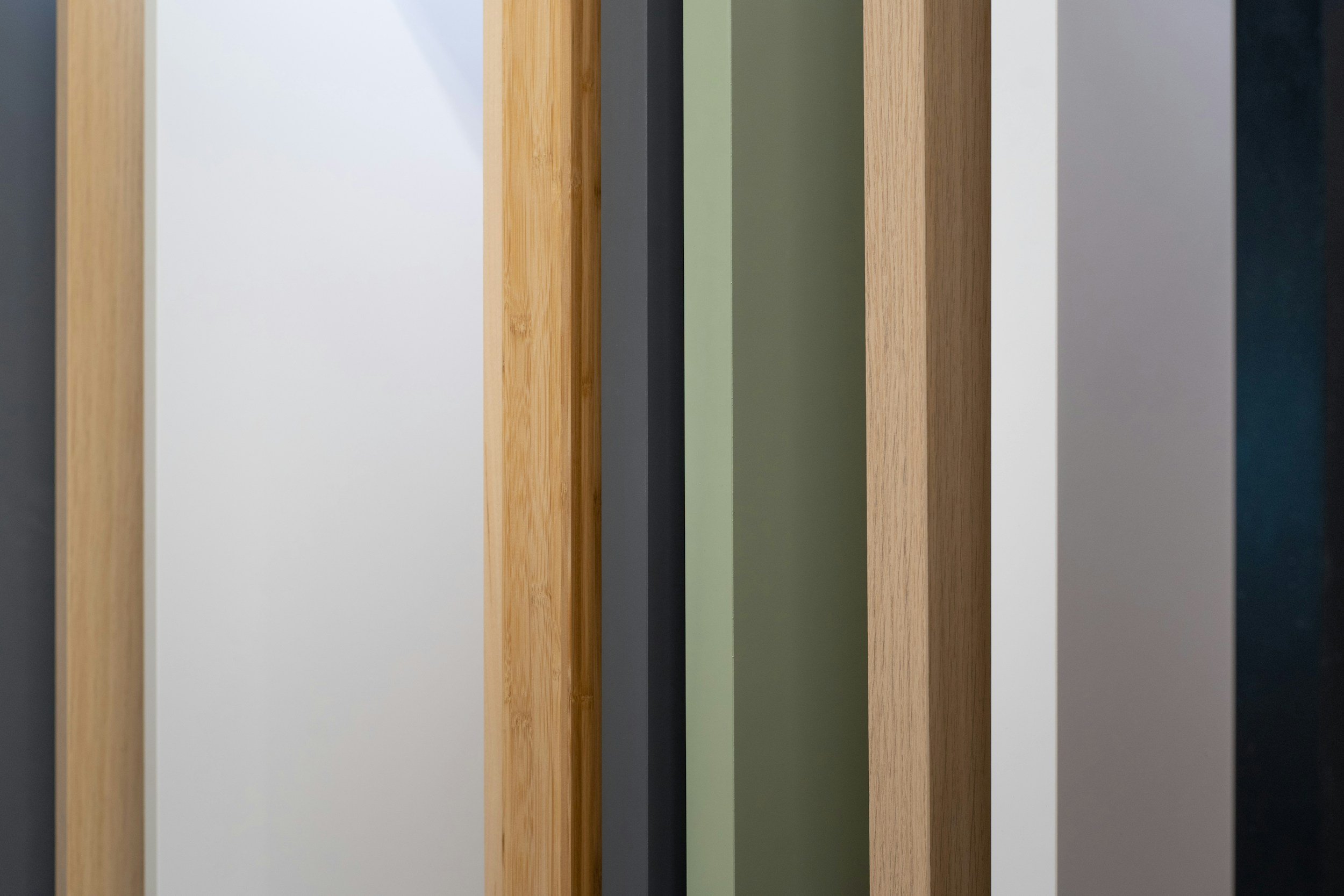 Various vertically aligned wooden, painted, and textured samples, including shades of white, green, black, gray, and natural wood.
