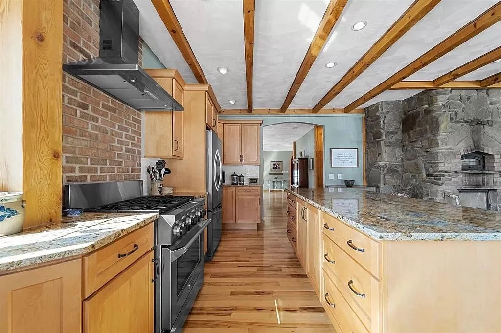 Modern kitchen with wooden cabinets, granite countertops, stainless steel appliances, and a stone fireplace in the background.