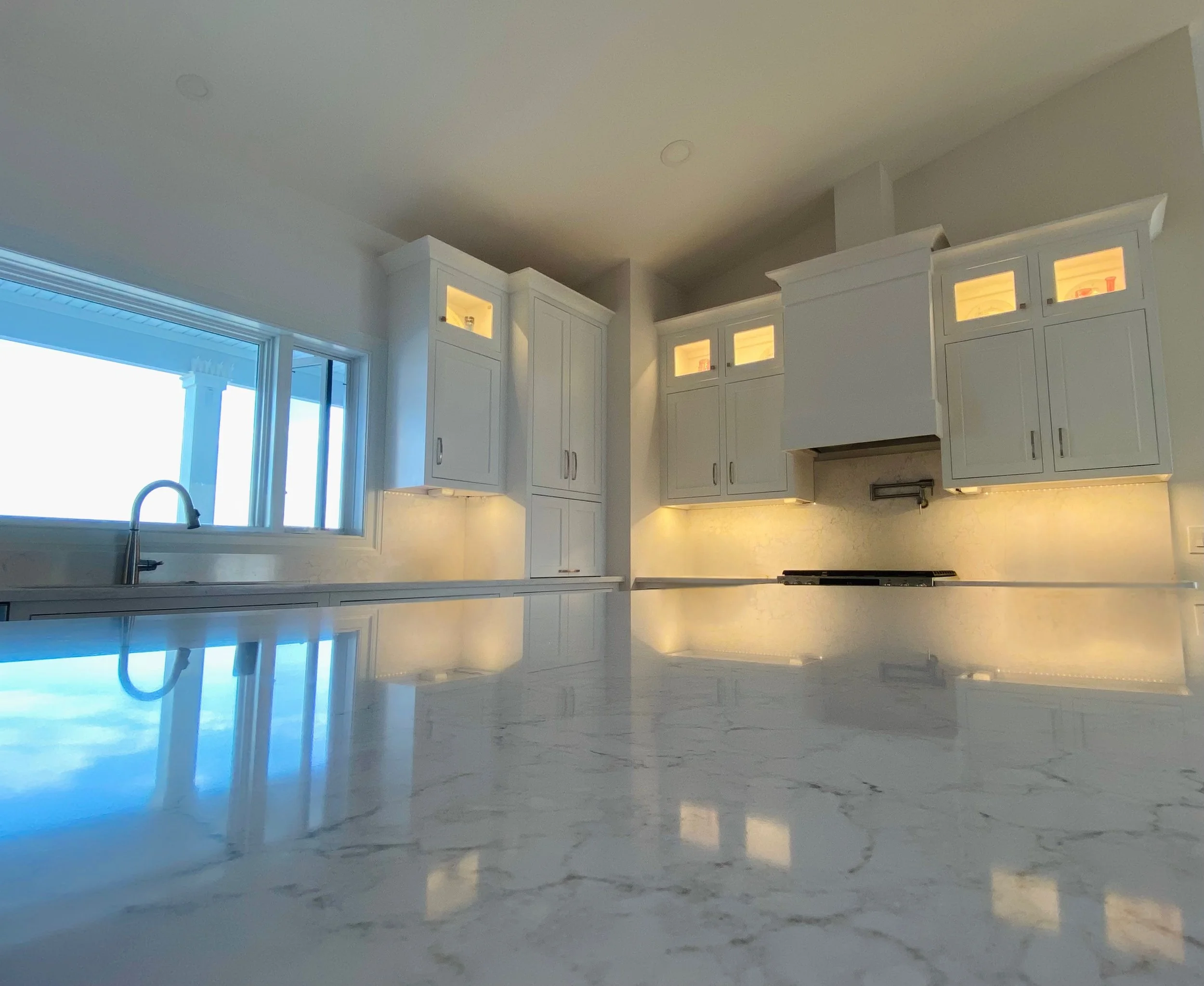 Kitchen with white cabinets, marble countertop, and large window showing blue sky outside