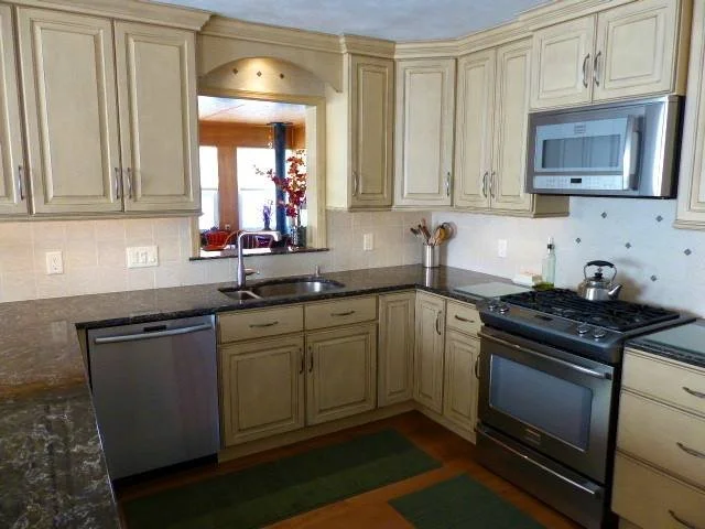 Kitchen with cream cabinets, black countertops, and stainless steel appliances, including a microwave, stove, and dishwasher.