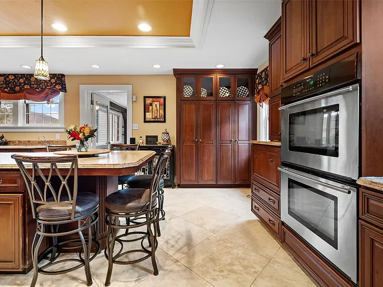 Kitchen with wooden cabinetry, a built-in oven and microwave, a kitchen island with barstools, and a window with a floral valance.