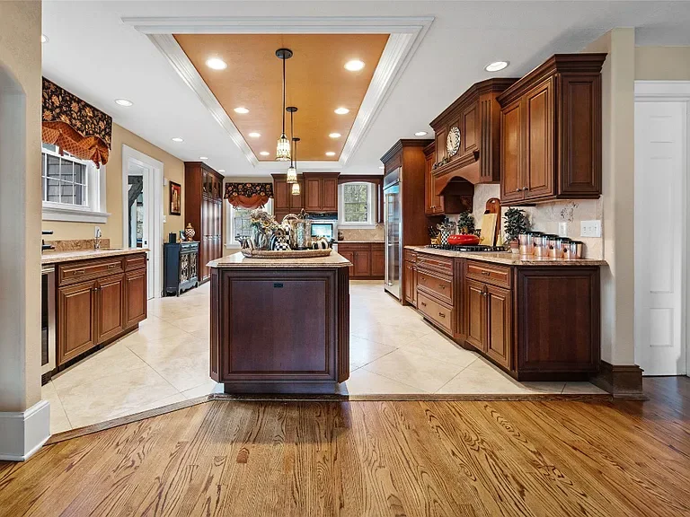 A spacious traditional kitchen with wooden cabinets, a central island, tiled flooring, and recessed lighting.