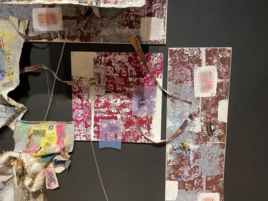 Mixed media artwork with torn paper, fabric, and wires on a dark background, featuring floral and abstract patterns in red, pink, beige, and yellow.