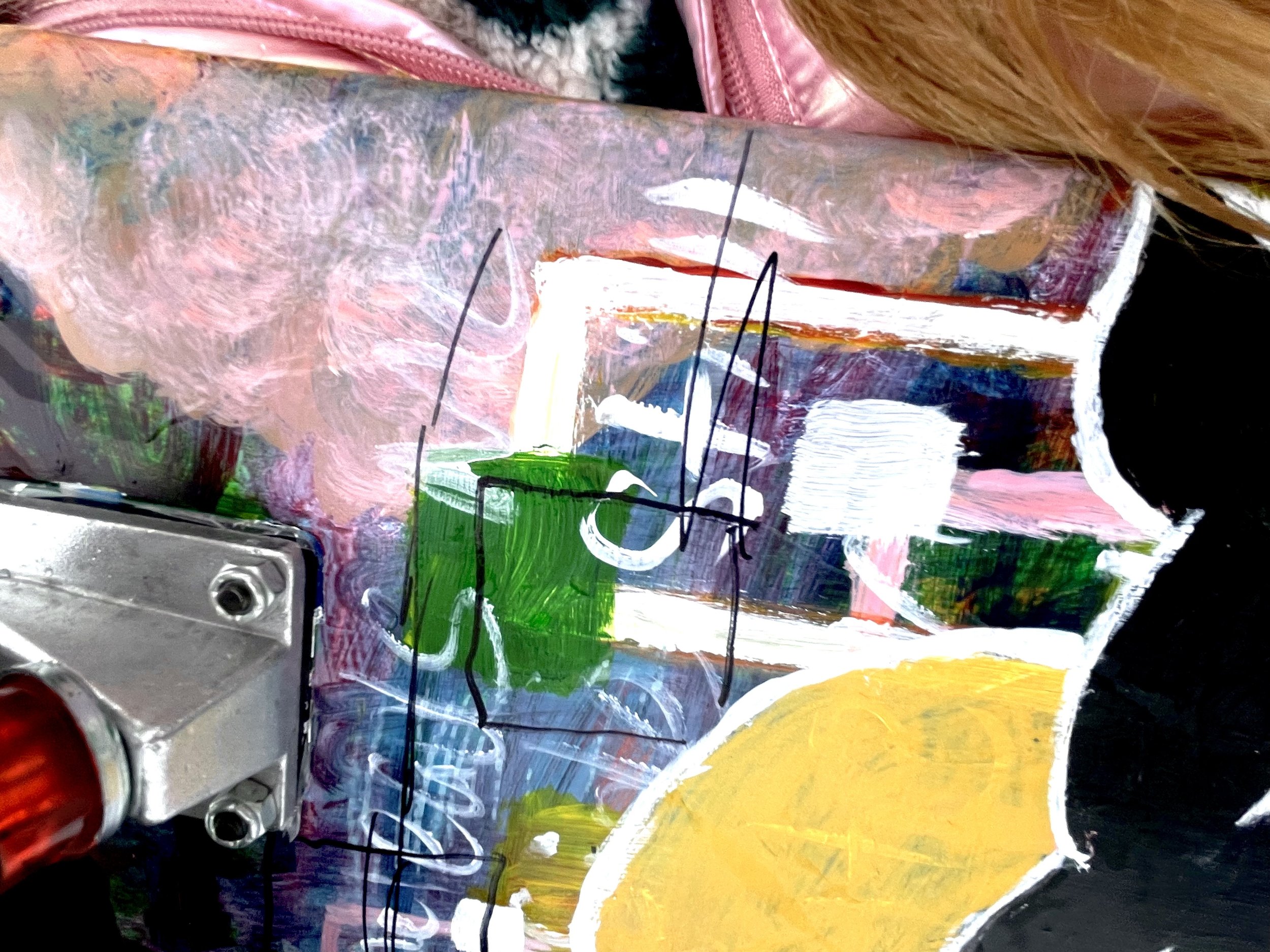 Close-up of an abstract painting with pink, green, yellow, black, and white brushstrokes, and black lines, on a surface near a metal mechanical part.