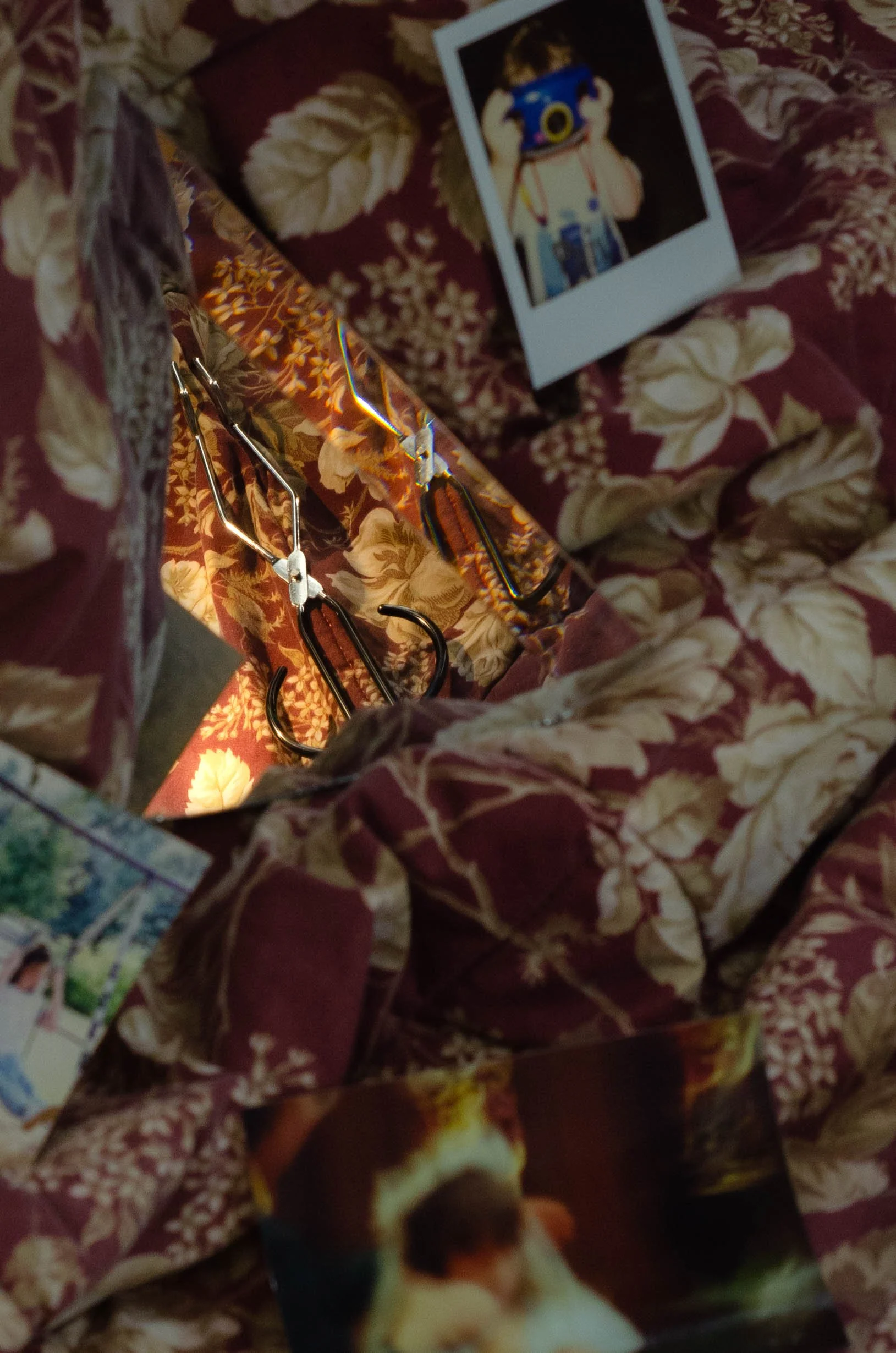 A mirror reflecting a floral-patterned interior with a photograph of a child taking a picture with a camera, and several photographs placed on a floral fabric surface.