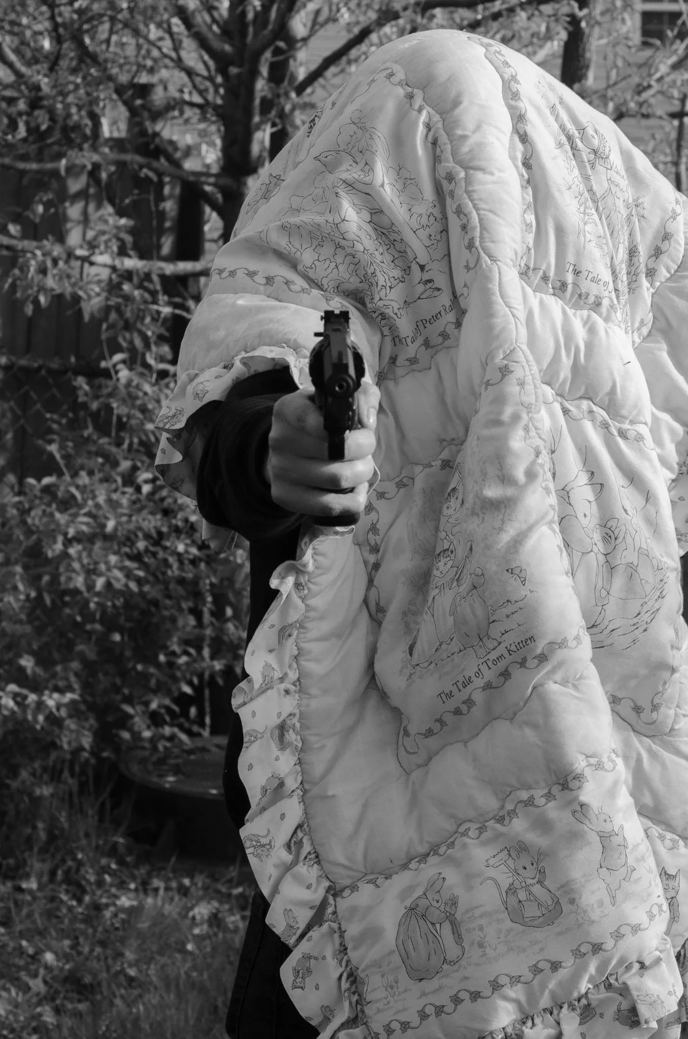 A person in a quilted jacket holding a gun, standing outdoors with trees in the background.