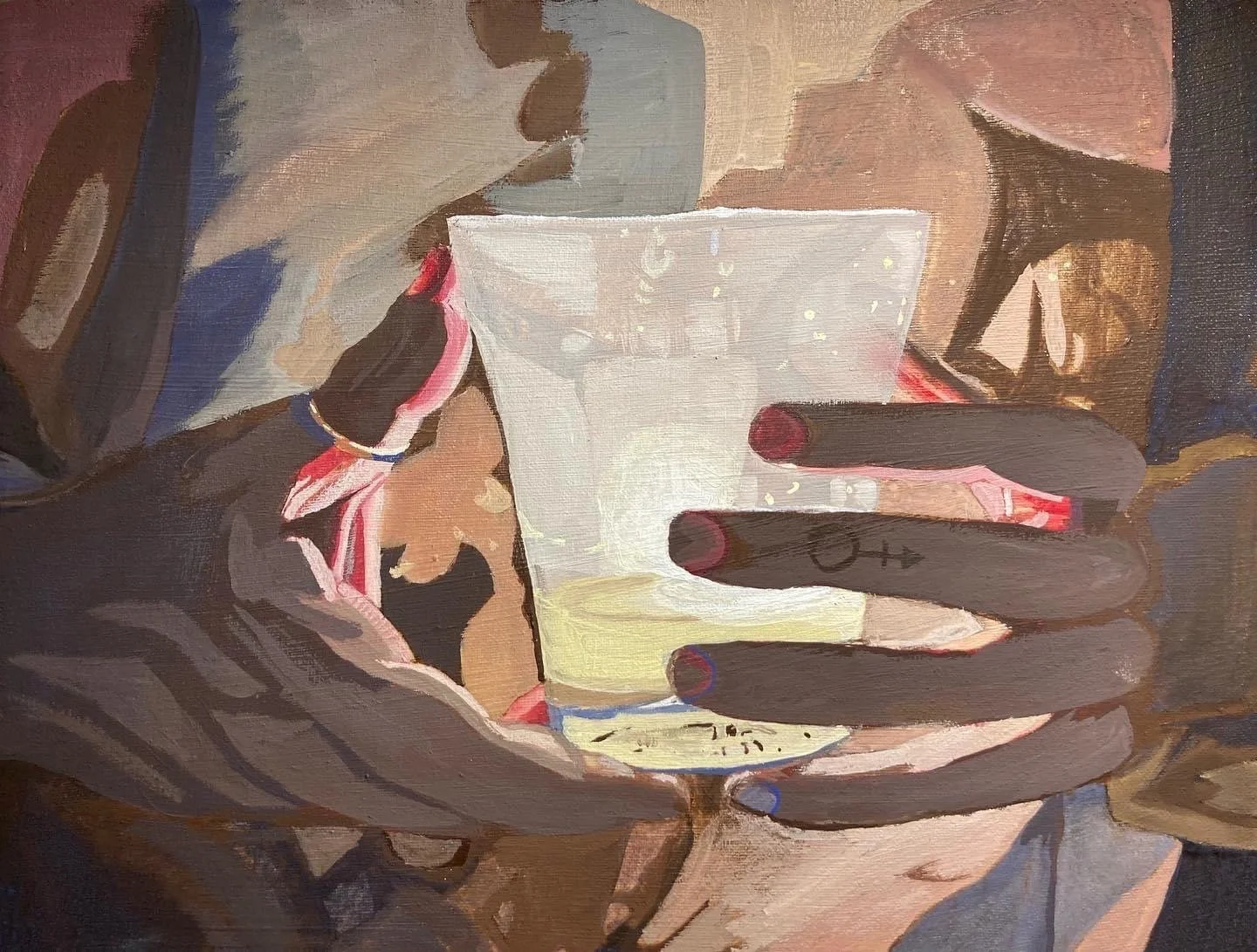 A person with dark skin and colorful painted nails is holding a glass of a yellowish beverage, possibly a cocktail or juice, with both hands. The person is wearing a brown sweater and has a bracelet on one wrist.