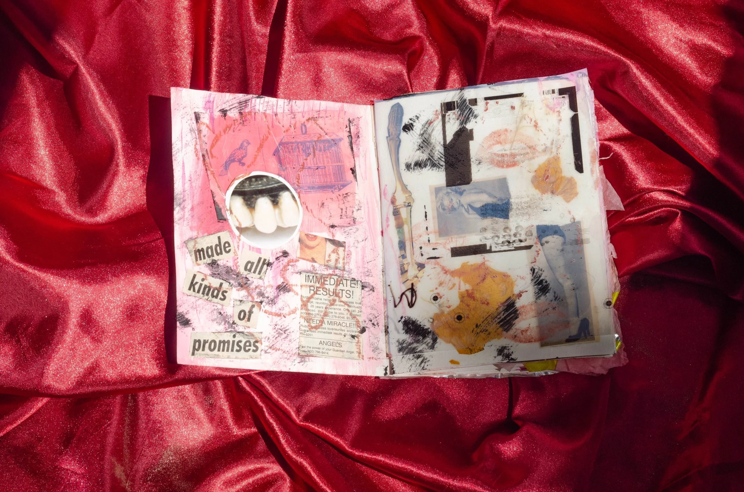 An open art journal on red satin fabric containing collaged images, drawings, and text, including a cutout of teeth, phrases like 'made all kinds of promises,' and various layered artwork.