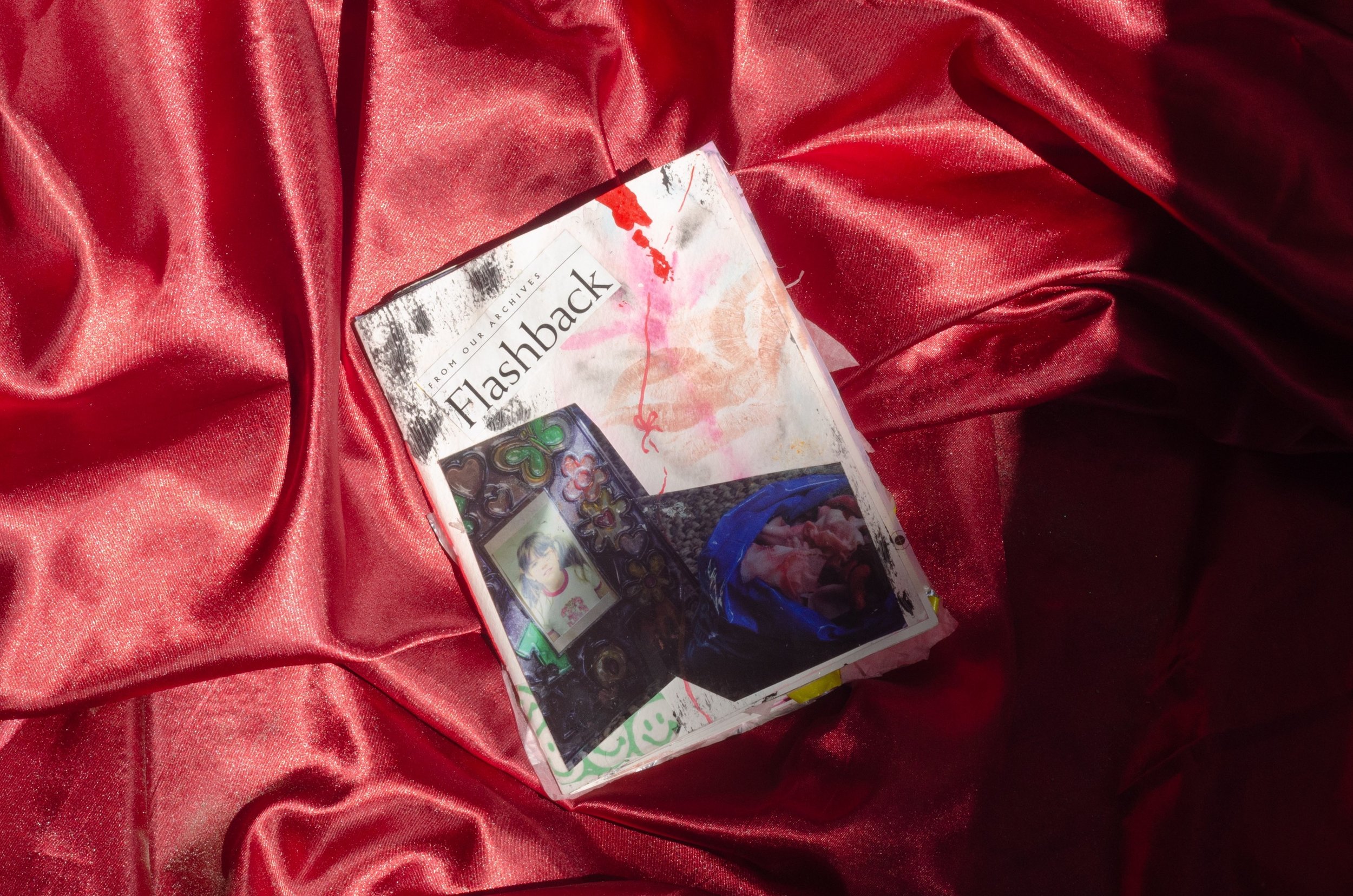 A photo of a deck of cards with the brand name 'Flashback' on a red satin fabric. The deck features colorful artwork and a camera image on the front.