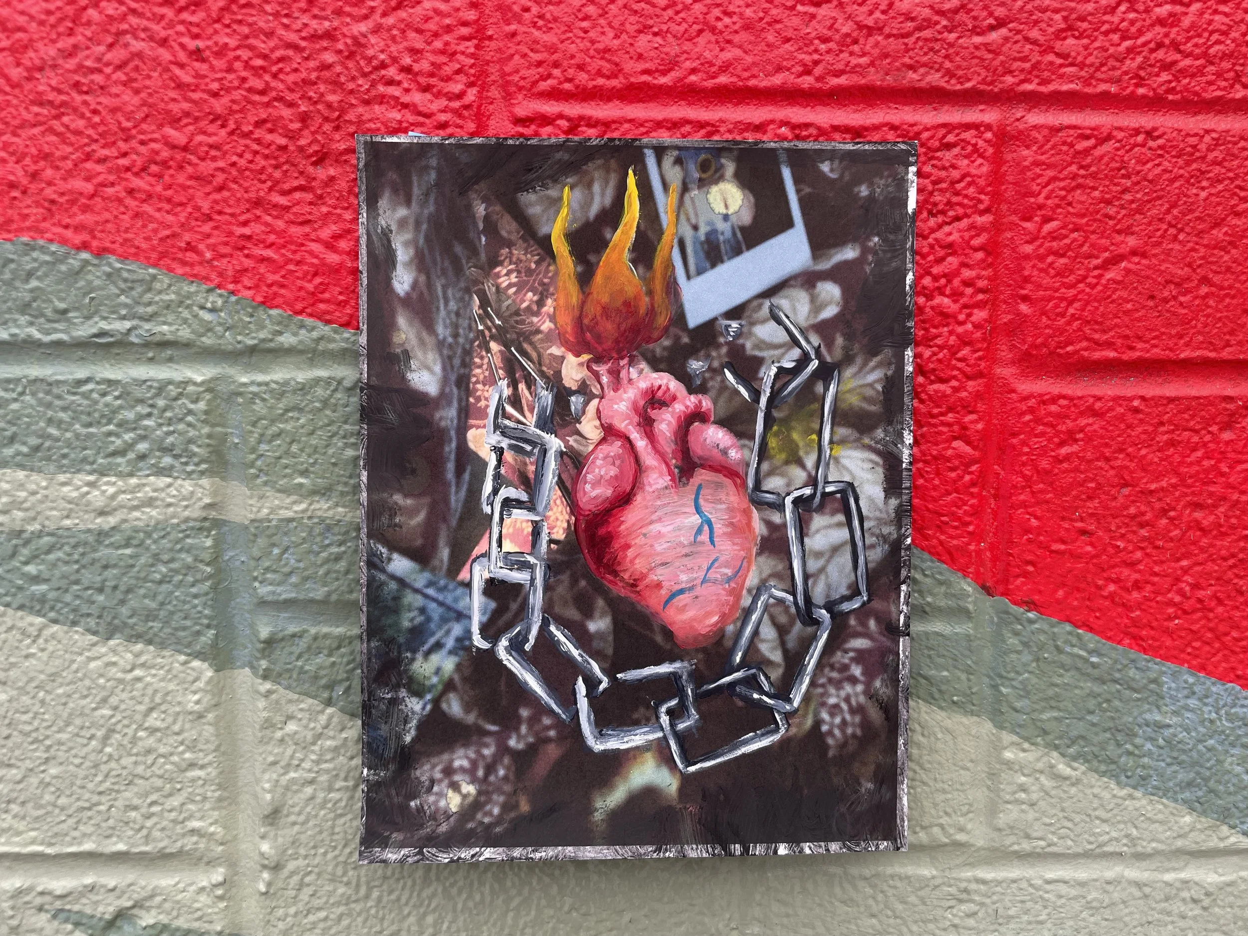 A colorful mixed-media artwork of a realistic human heart with flames on top, surrounded by a chain linked in a circle, against a textured background of graffiti-style wall.