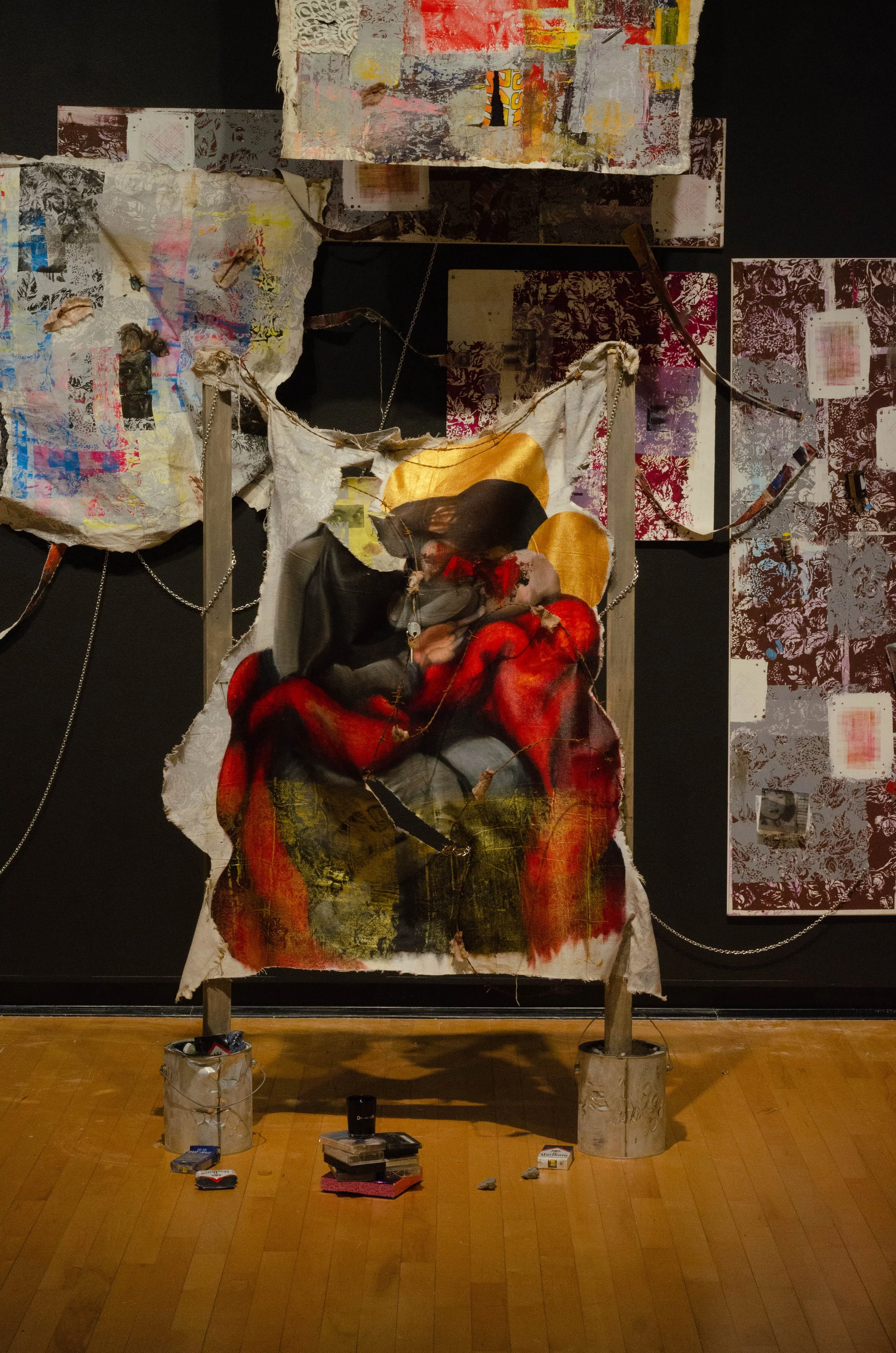 Mixed media art installation featuring torn fabric with an image of two embracing women, set against abstract painted backgrounds.