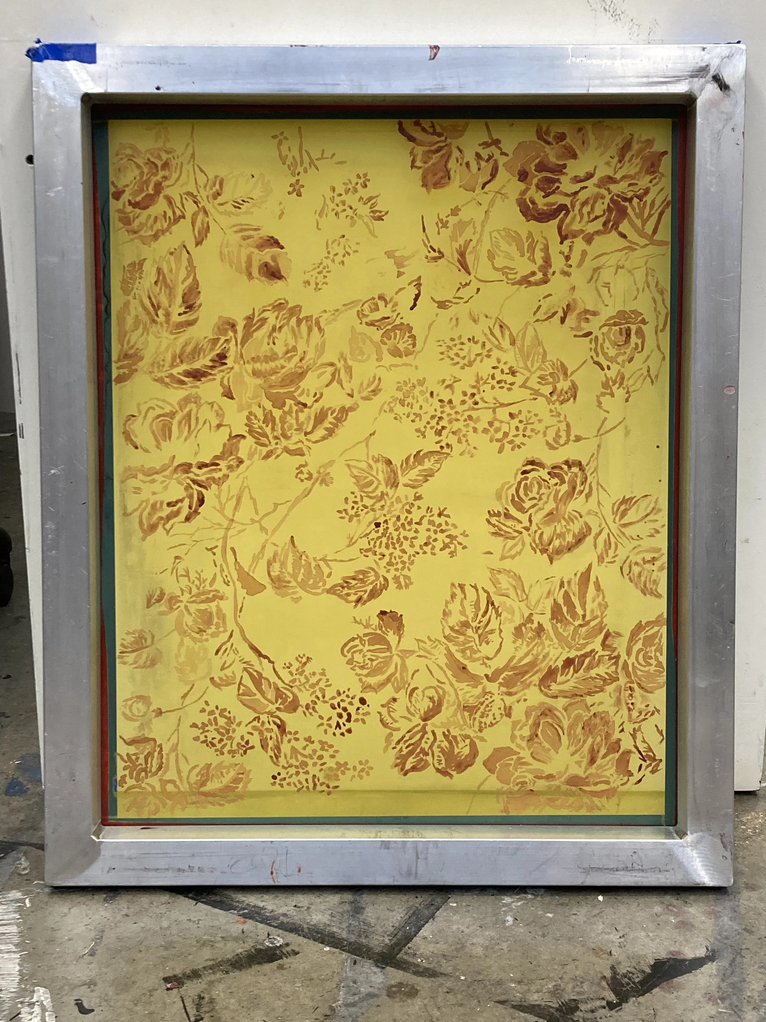 A decorative mirror with a floral design in yellow and brown, framed with a metallic silver border.