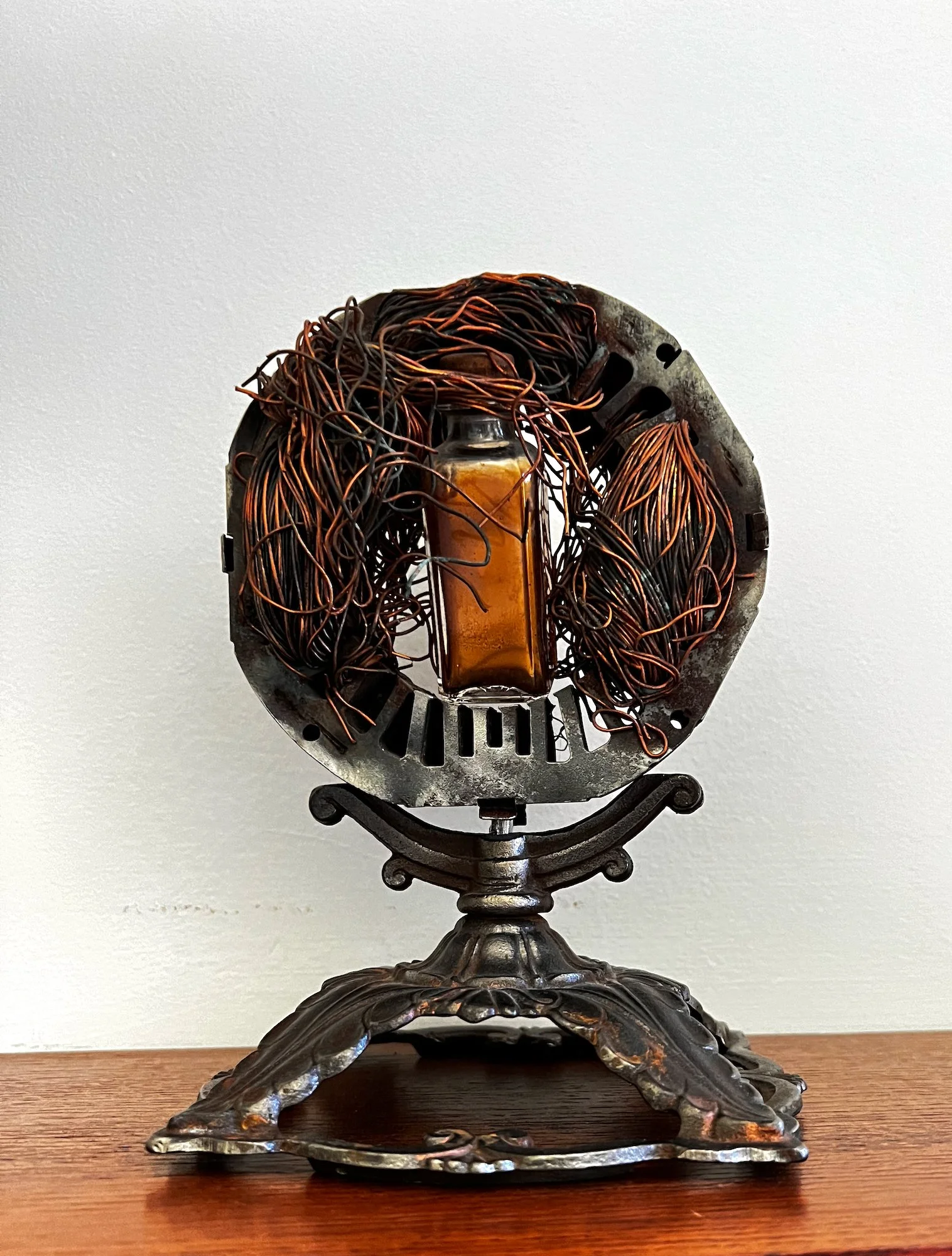 Vaccine - Inspired by the use of vaccines to prevent the spread of the covid virus. Vintage cast iron lamp base, electric motor part, steel, vintage glass bottle. 8.25” x 6” x 6”. 2020.