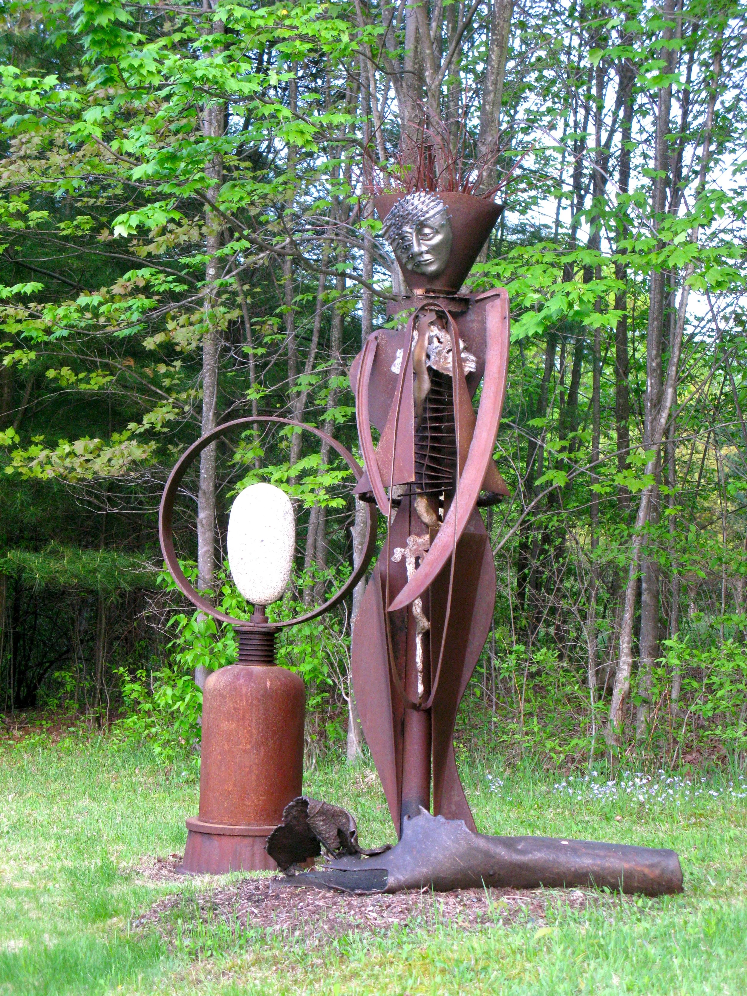 Agrarian  - Inspired by the agrarian way of life in the rural upstate NY. Much of the steel in my collection has come from abandoned farms and outdated farm equipment. Welded salvaged steel, modeled clay face with horse
shoe nails. 8’5” x 3’ x 3’ ( a