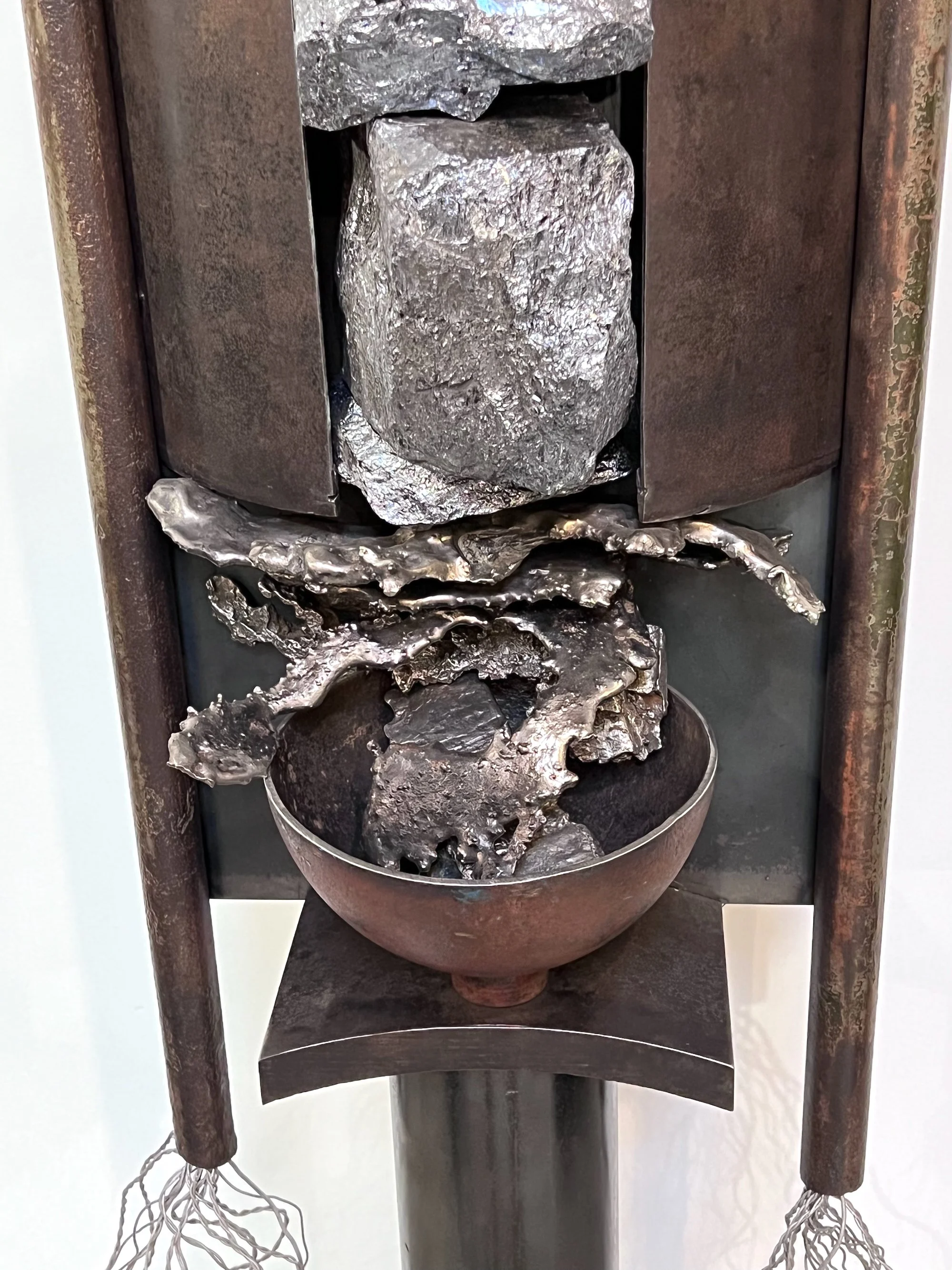 Dispenser - Inspired by earth’s natural resource, Silica ore and the effect mining for natural resources has on the environment. Welded steel, deconstructed propane tank, cow stanchion posts, cast stainless steel, aluminum wire, silica ore. 76” x 16”