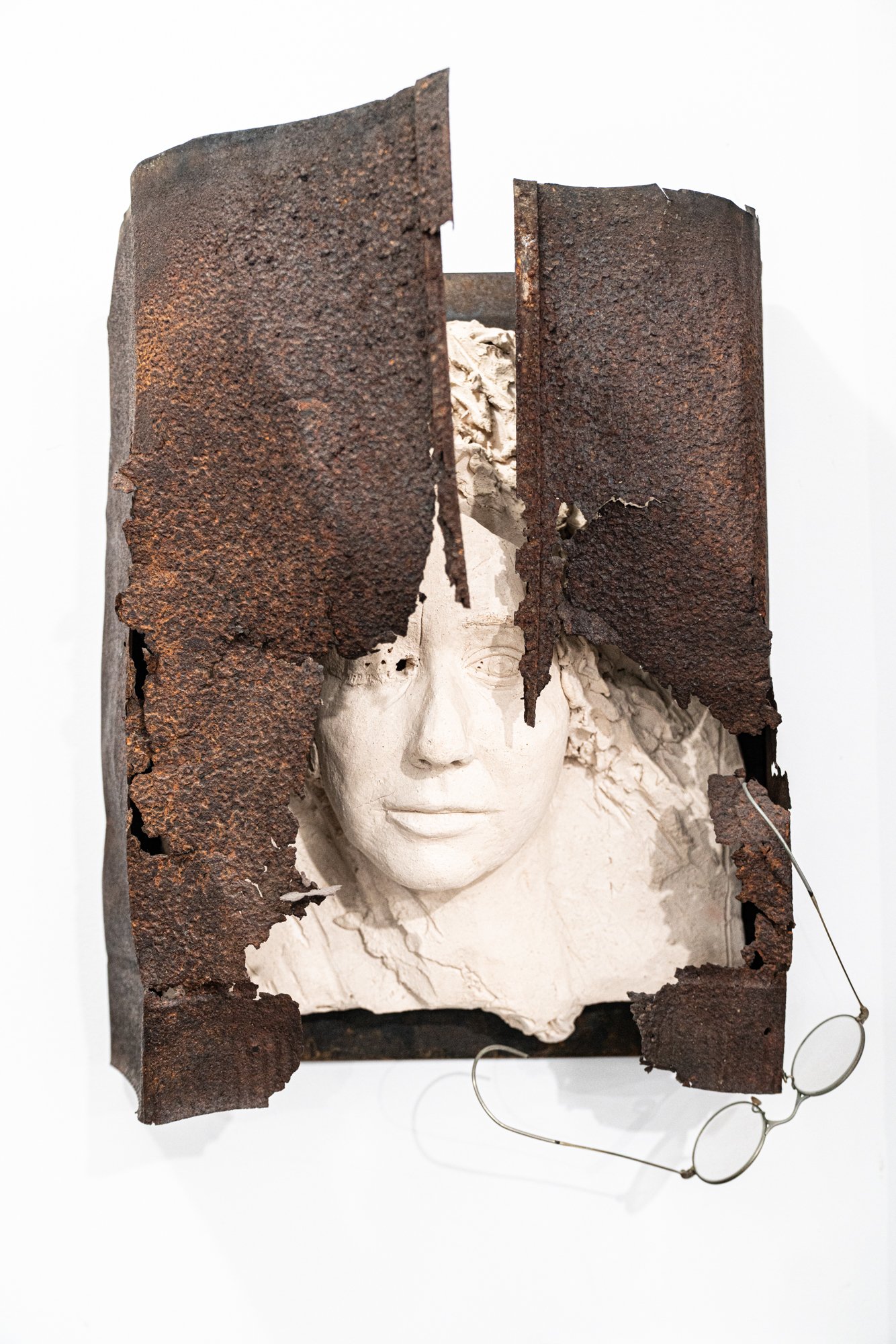 Self Portrait  - Vision Shock - Self-portrait after discovering an eye issue. Modeled clay face relief, rusty steel, glasses. 28” x 18” x 8” 1988