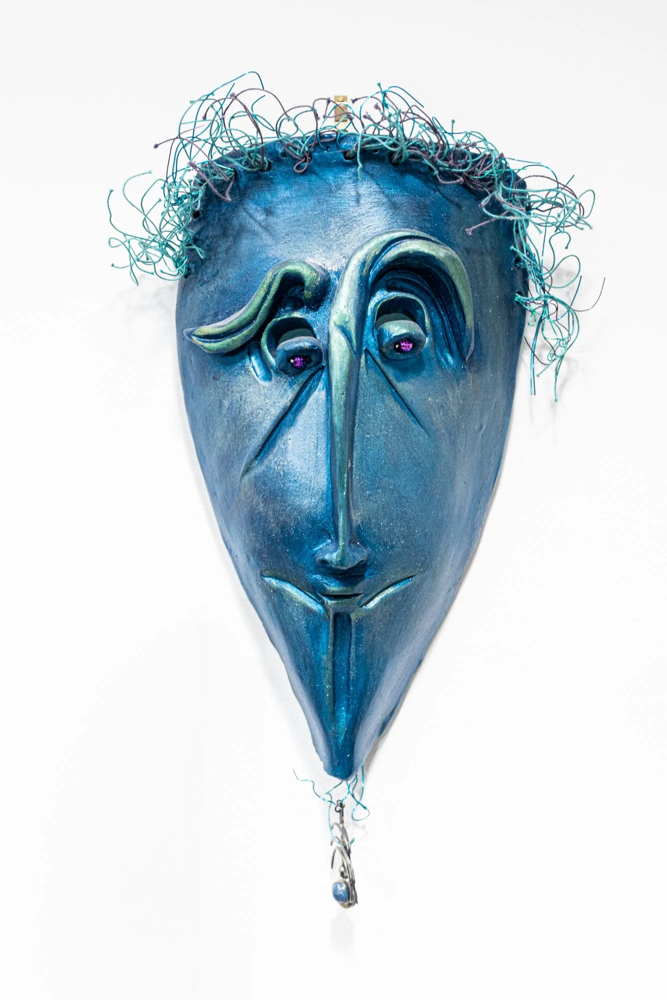 Blue Man Mask (Wire Hair) - Intuitively modeled. Low fire clay, painted and adorned with blue wire, purple beads for eyes, silver charm. 15” x 8” x 3” 