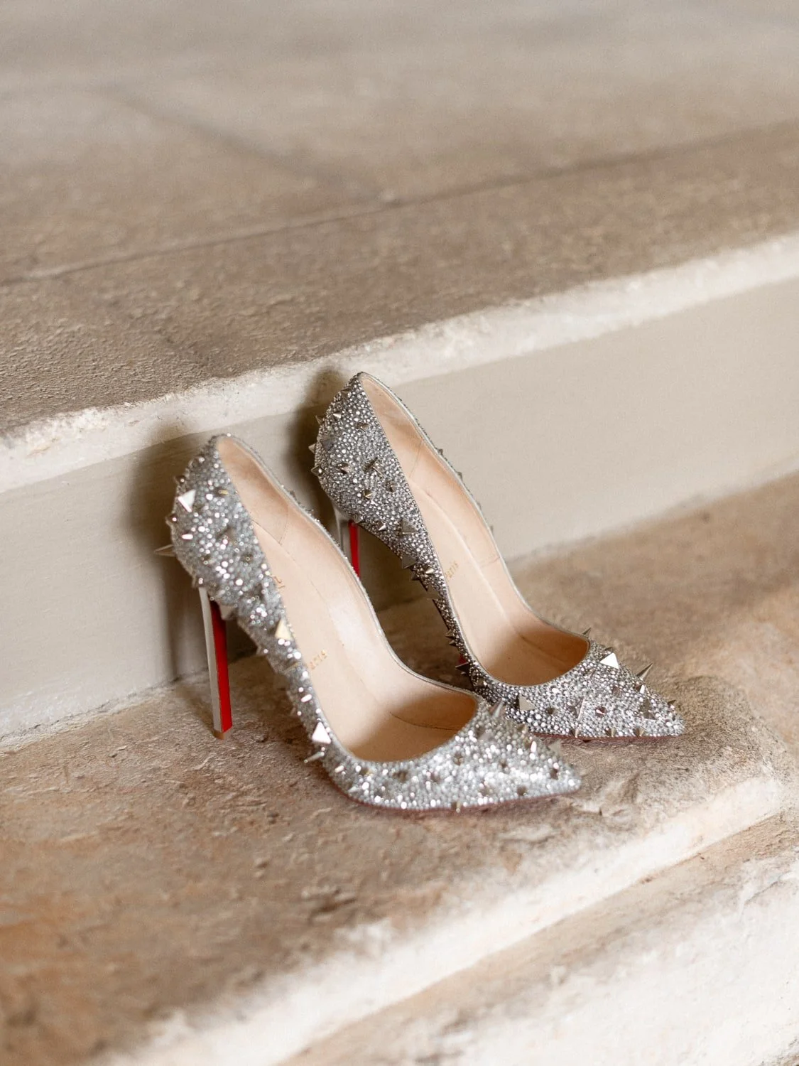 Silver studded high-heeled shoes with red soles on stone steps.