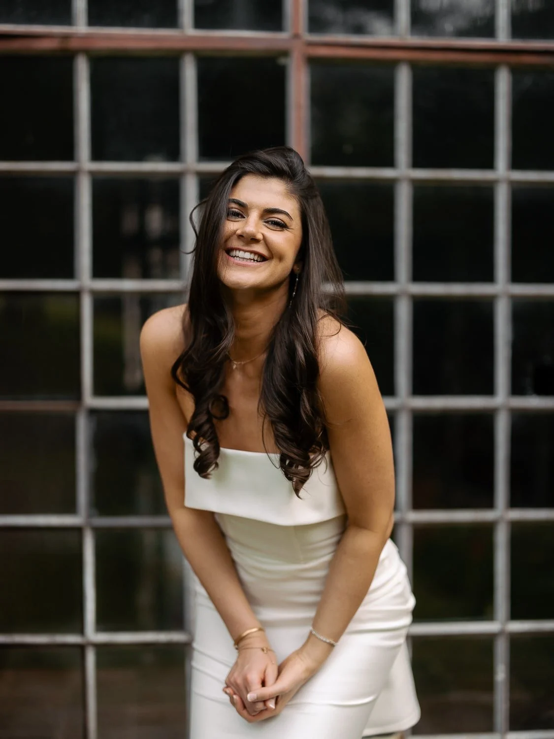 Smiling woman in white dress posing in front of a window grille.