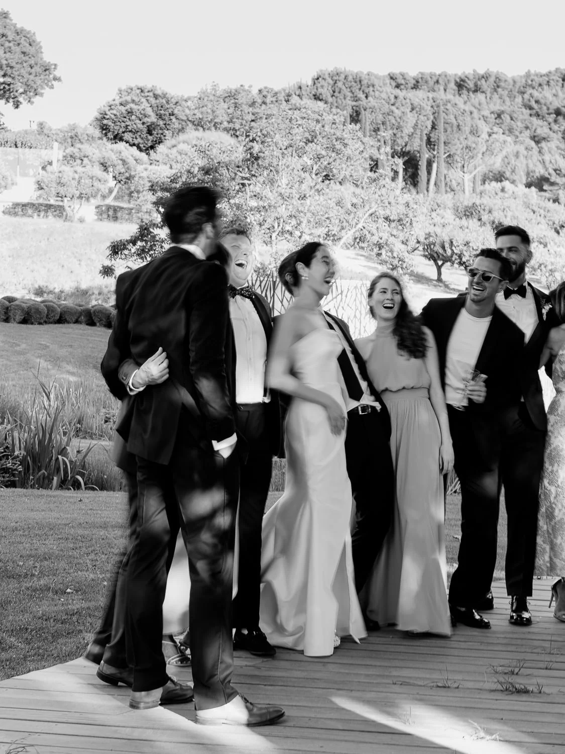 Group of people dressed in formal attire celebrating outdoors in black and white photo.