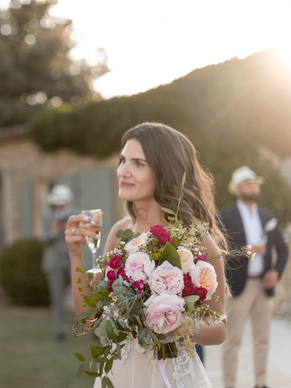 Woman holding a bouquet of flowers and a glass of champagne at an outdoor event.