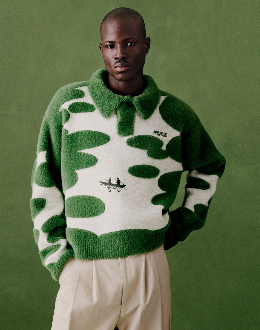 A man wearing a green and white fuzzy camouflage-patterned sweater, standing against a matching green background.