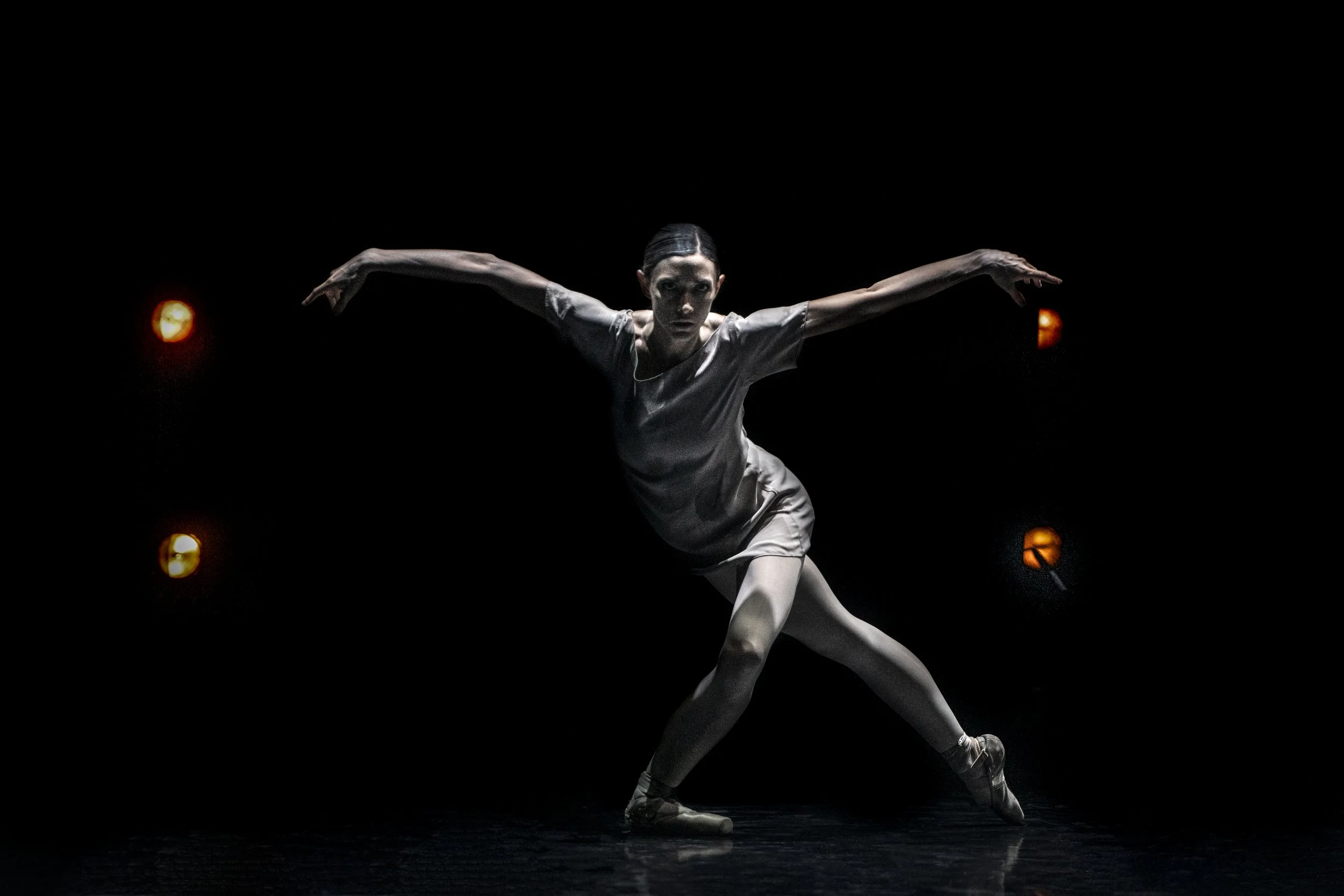 A female ballet dancer performing on stage with arms outstretched and lighting creating a dramatic effect.