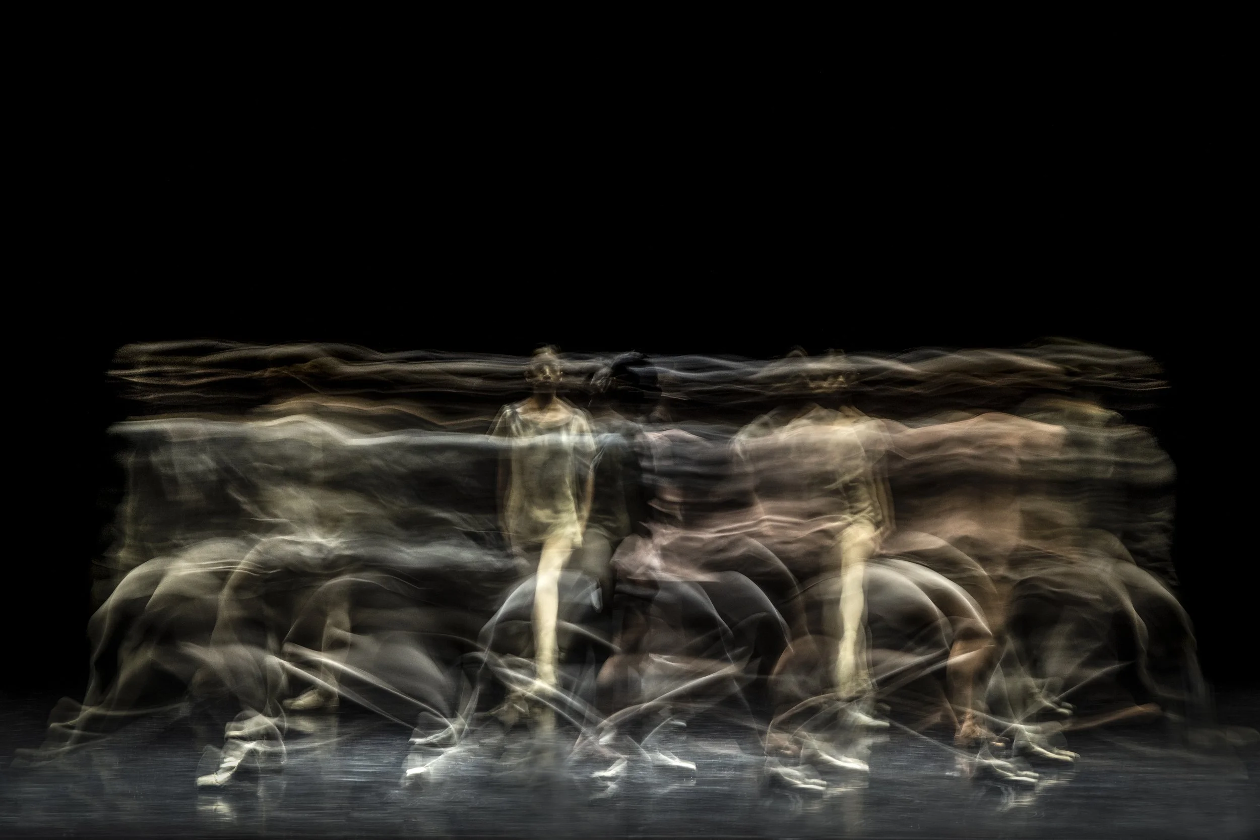 Blurry motion image of multiple people walking, with some standing still, in a dark environment.
