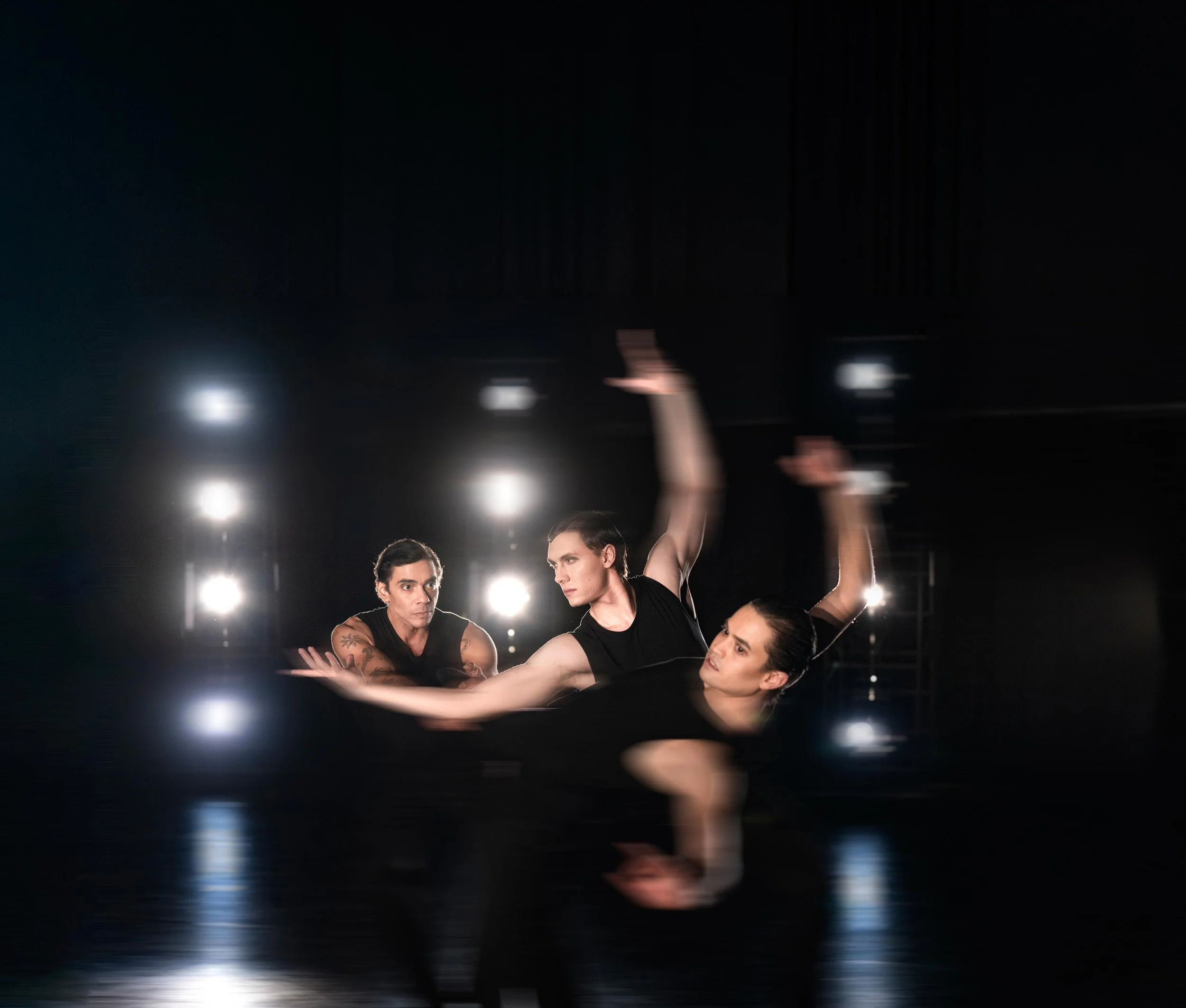 A group of young dancers performing on stage, with one dancer bending backwards and extending her arms, while the others stand in formation behind her, all dressed in matching costumes under stage lighting.