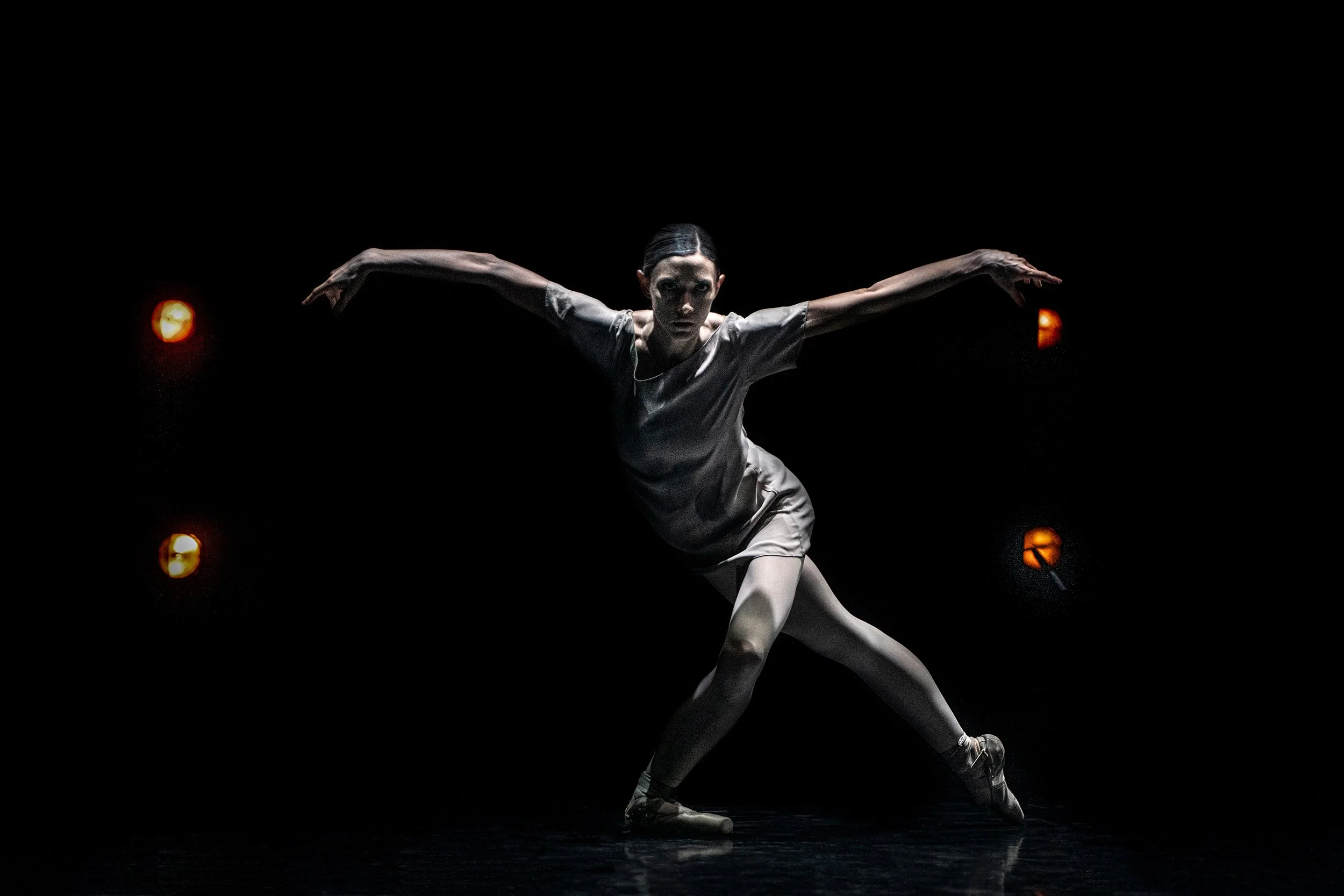 A female ballet dancer performing on stage with arms outstretched and lighting creating a dramatic effect.