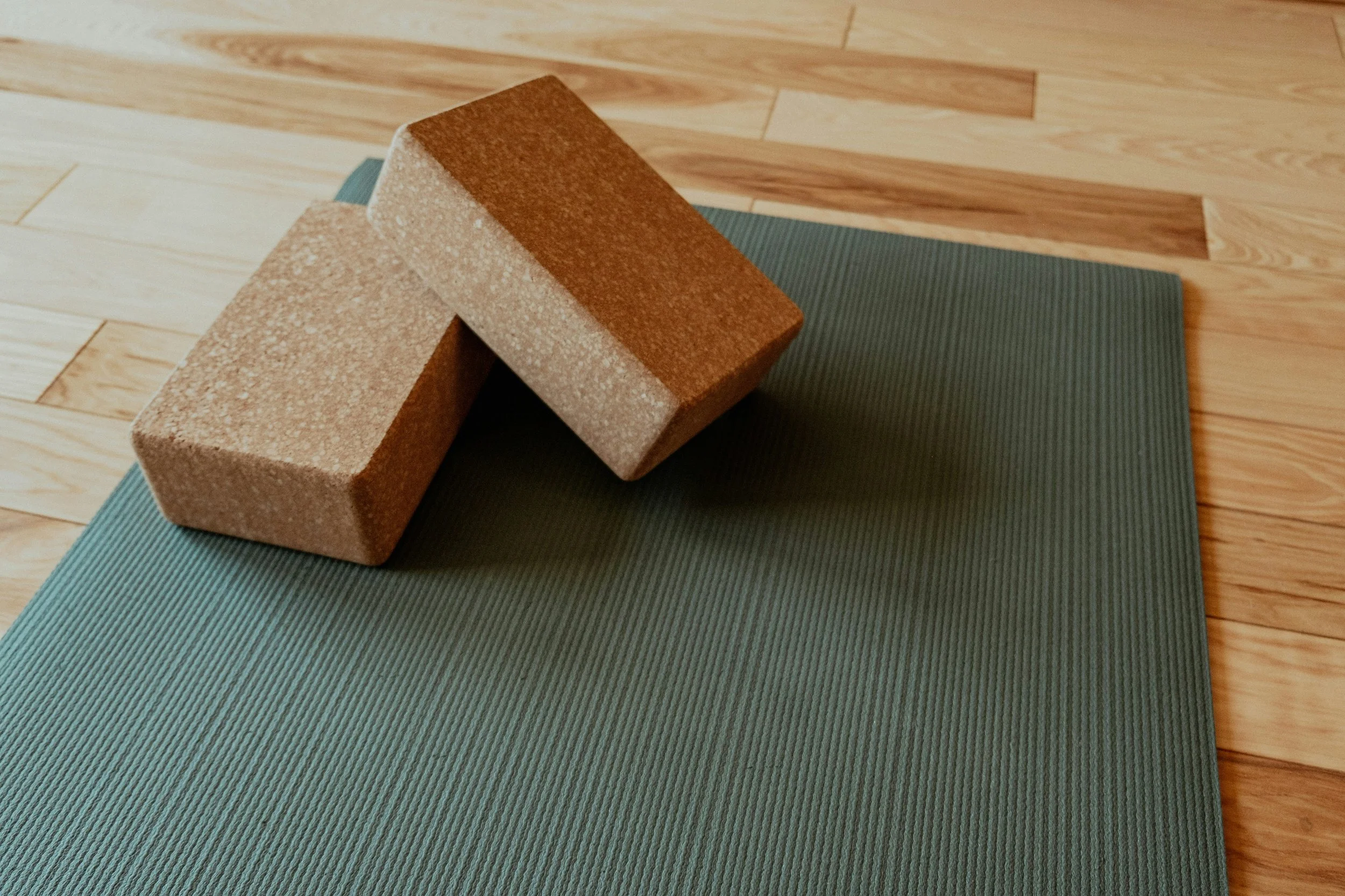 Two yoga bricks placed on a green yoga mat on a wooden floor.