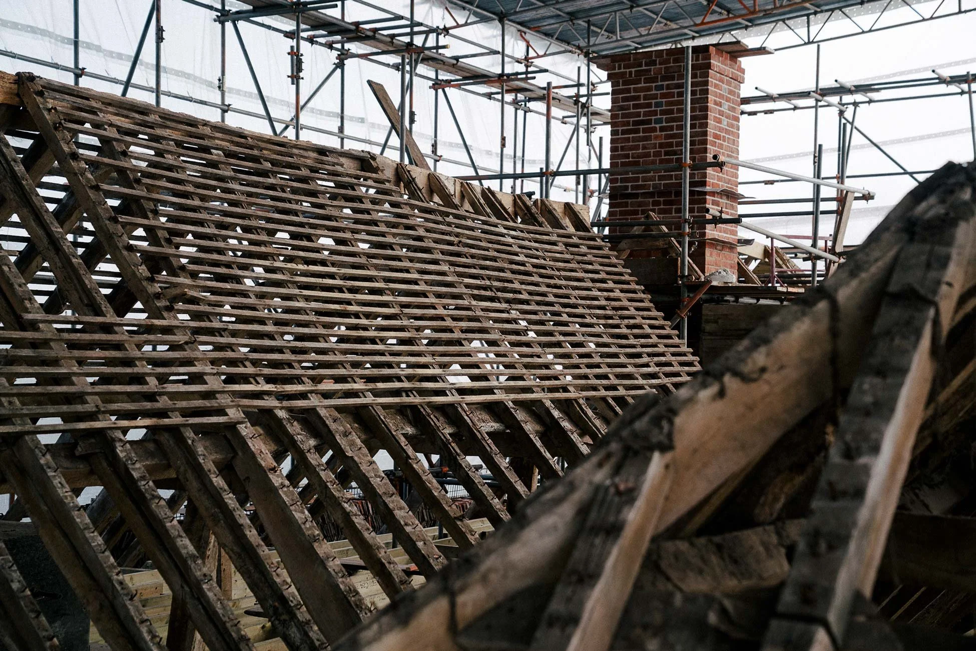 Construction site with scaffolding, a brick chimney, and wooden framework for a roof.