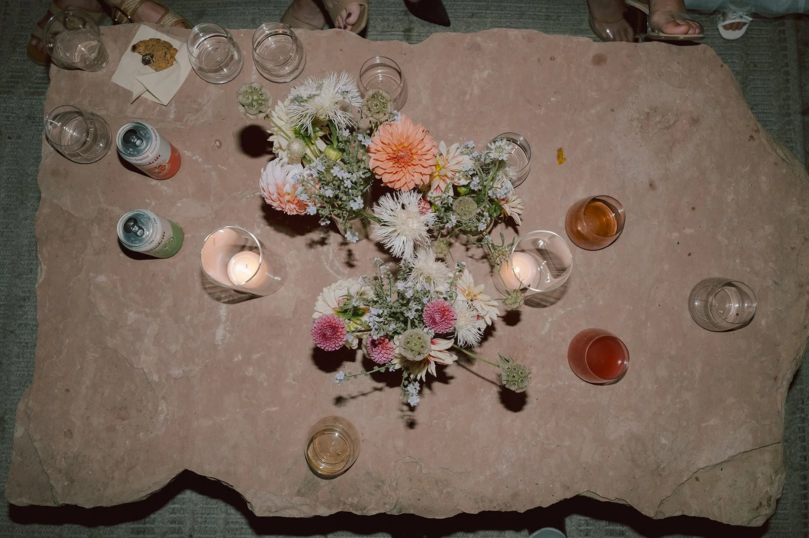 Top-down view of a dining table with a floral centerpiece, candles, drink glasses, and cans of soda.