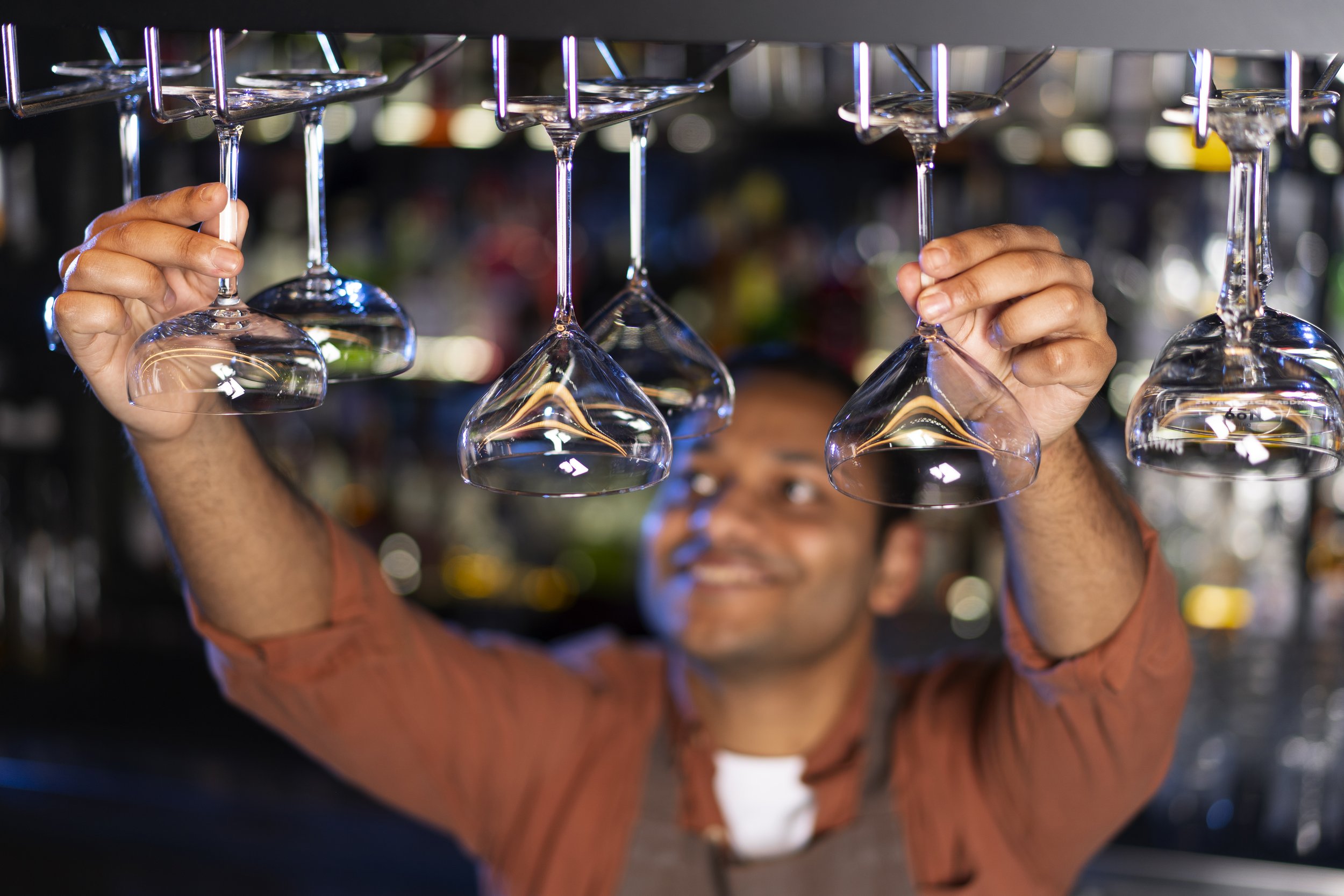 A bartender hanging upside down holding empty wine glasses by the stems, preparing to place them on a shelf.