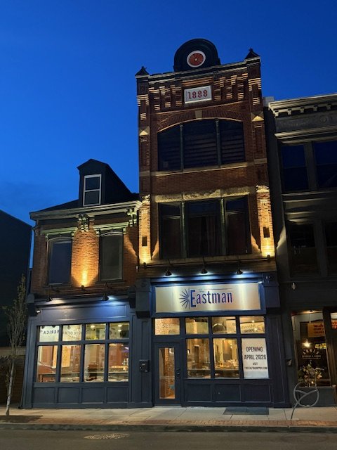 Vintage brick building at 520 East Ohio Street, lit at night, with a sign for The Eastman and an opening date of April 2026.