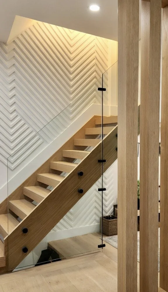 Interior staircase with wooden steps, a glass railing with black fasteners, and a decorative white geometric wall design. modern MDF slats design