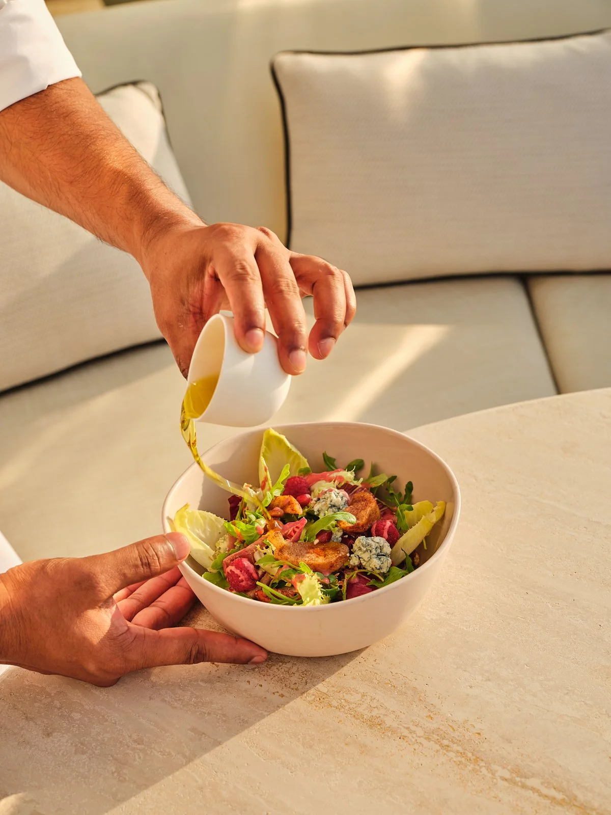 Person pouring salad dressing on a bowl of mixed greens and vegetables in a bright, modern setting.