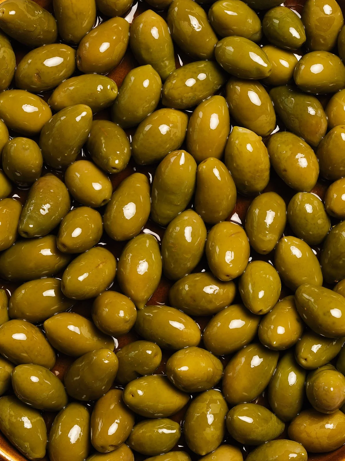 Close-up of green olives on a wooden surface.