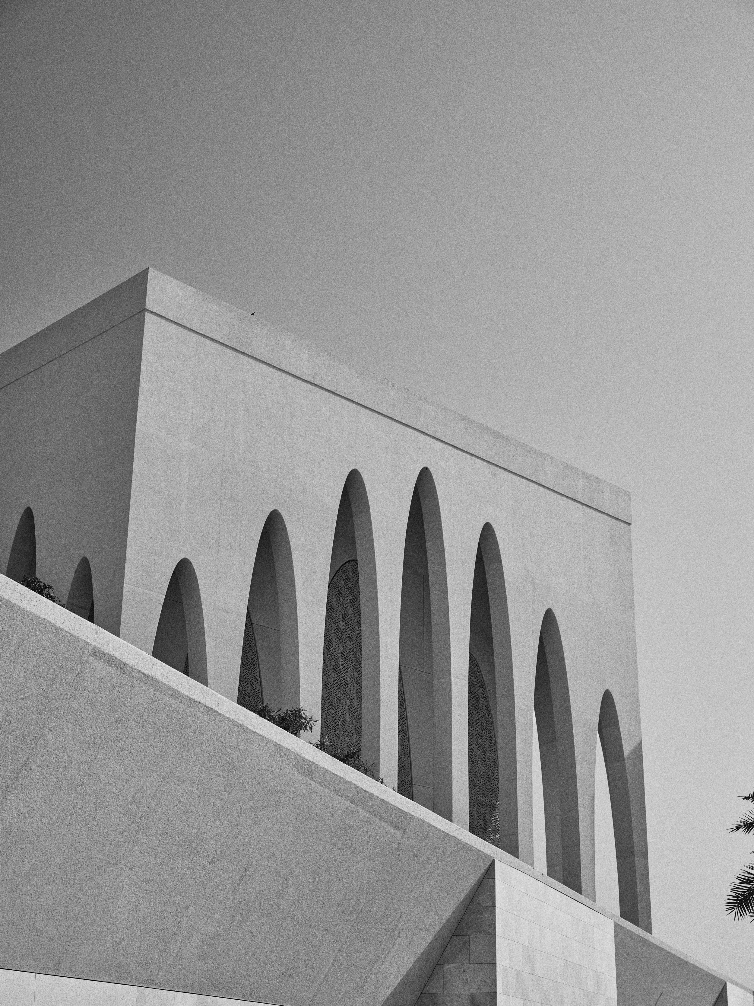 A modern building with large arches and a minimalist design, viewed from below against a clear sky.