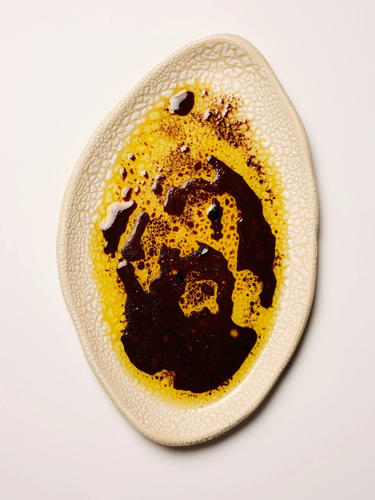 Close-up of a textured oval ceramic plate with a swirled pattern, containing olive oil, balsamic vinegar, and cracked black pepper.