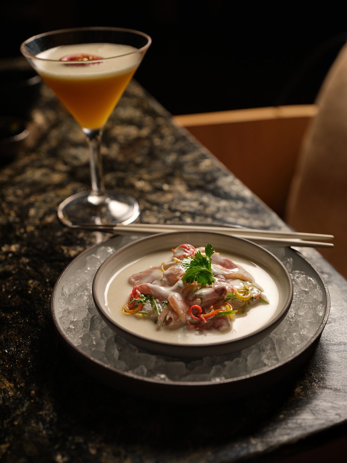 A cocktail drink and a bowl of ceviche on a dark granite counter.