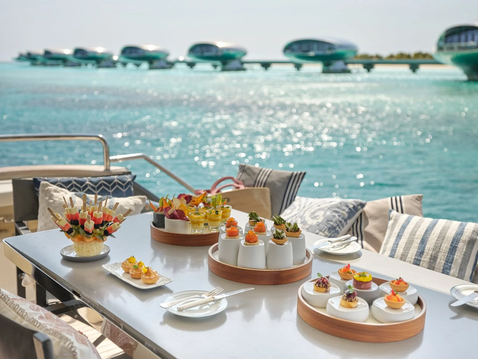 A table set with assorted appetizers and desserts on a waterfront patio overlooking the ocean and boats in the distance.