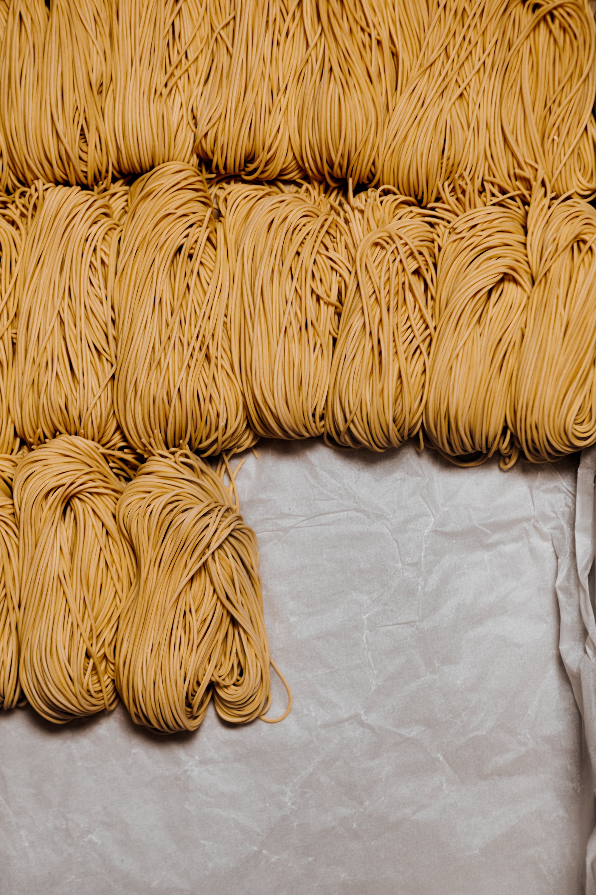 Batches of uncooked yellow noodles on parchment paper.